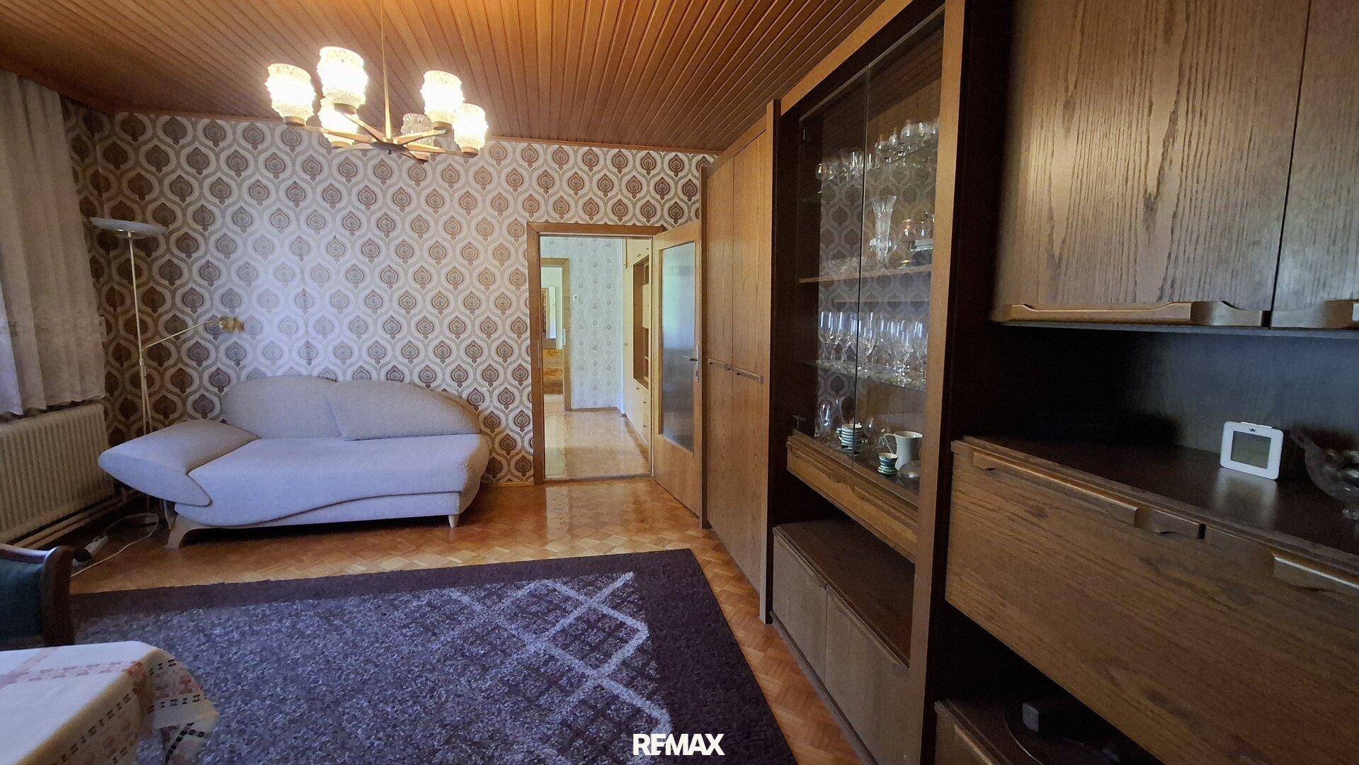 Wohnzimmer im Vintage-Stil mit gemusterter Tapete, Holzdecke und einem Sofa.