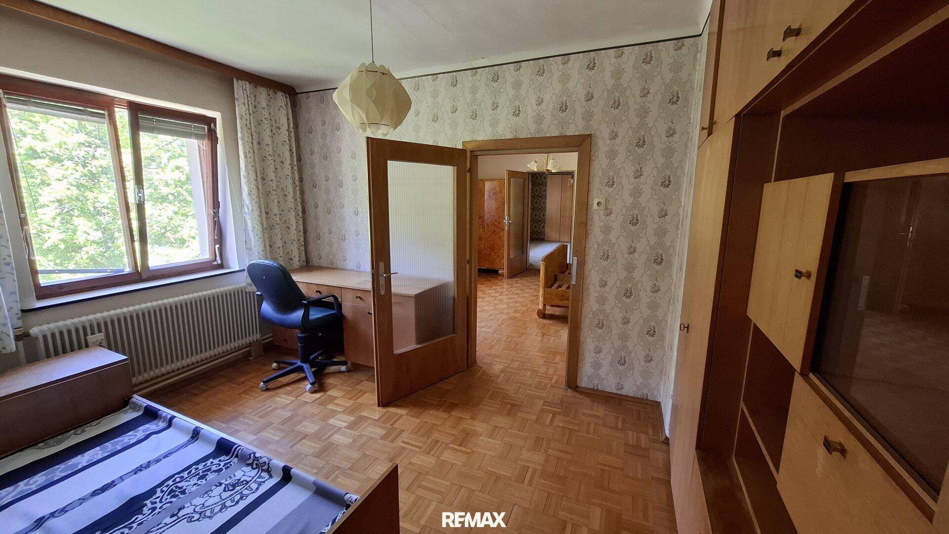 Schlafzimmer oder Büro mit Parkettboden, gemusterter Tapete und einem Schreibtisch.