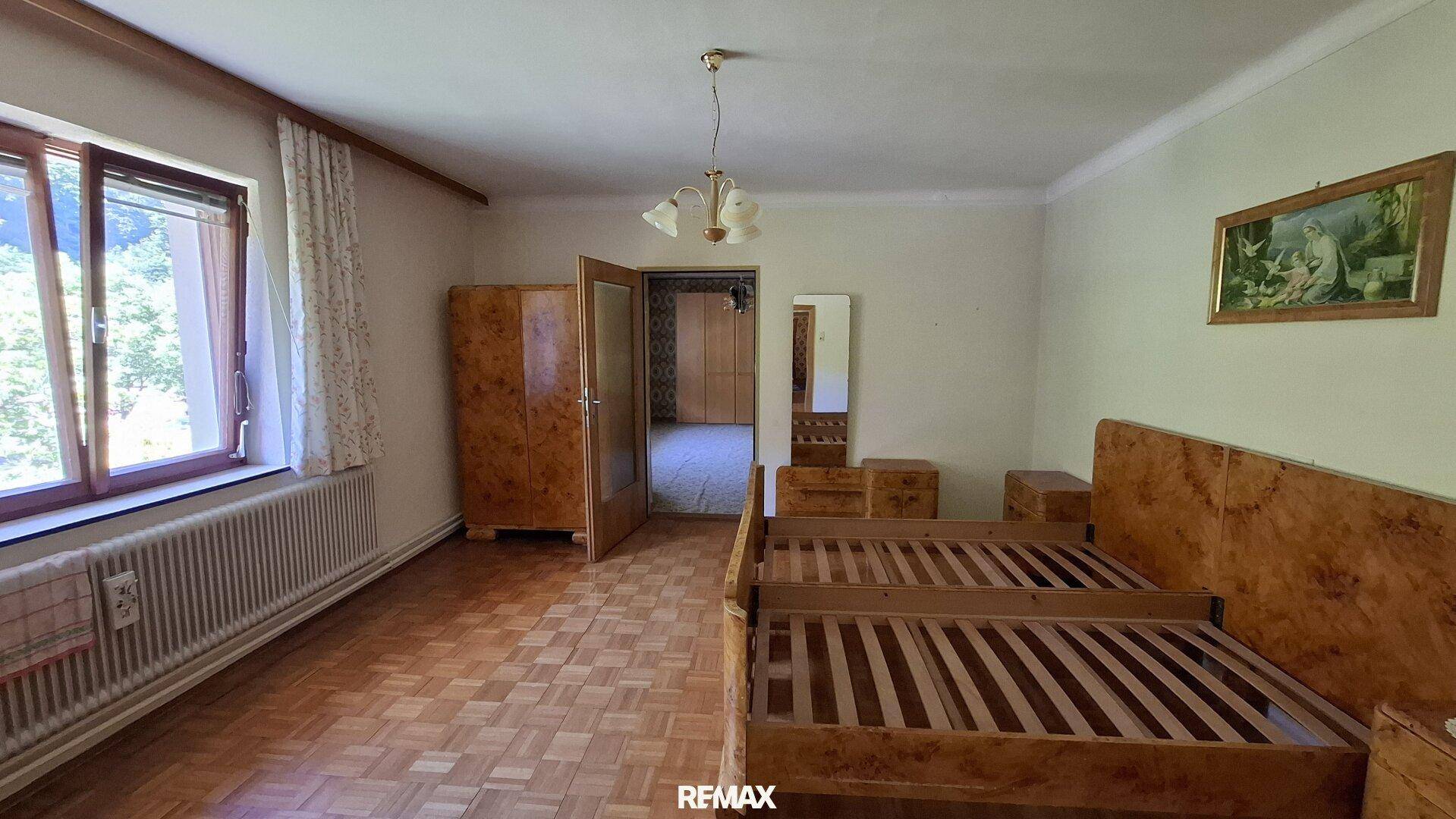 Schlafzimmer mit zwei Einzelbetten, Holzmöbeln und Parkettboden in einem älteren Stil.