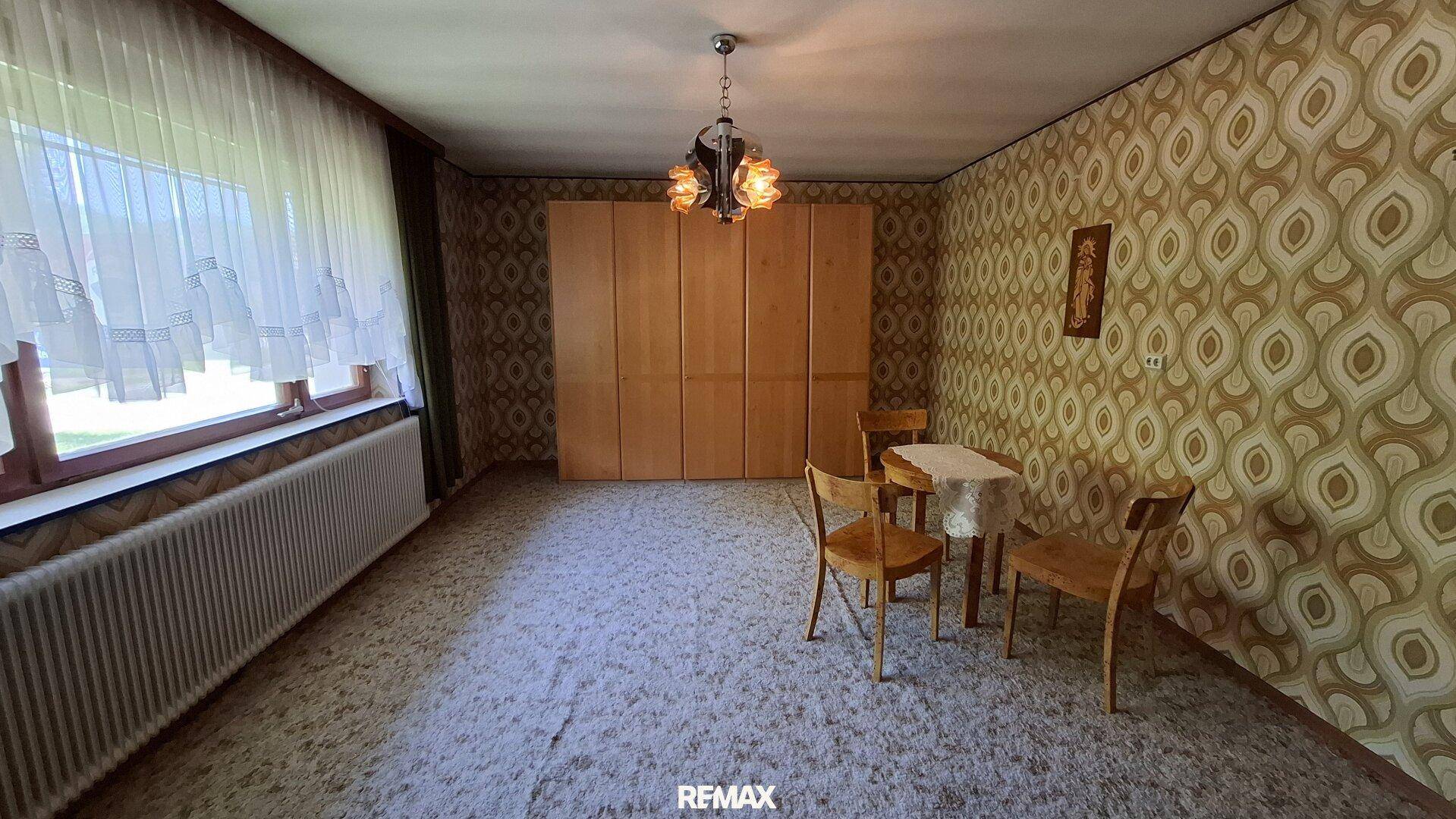 Zimmer mit Teppichboden, gemusterter Tapete und einem kleinen Esstisch.