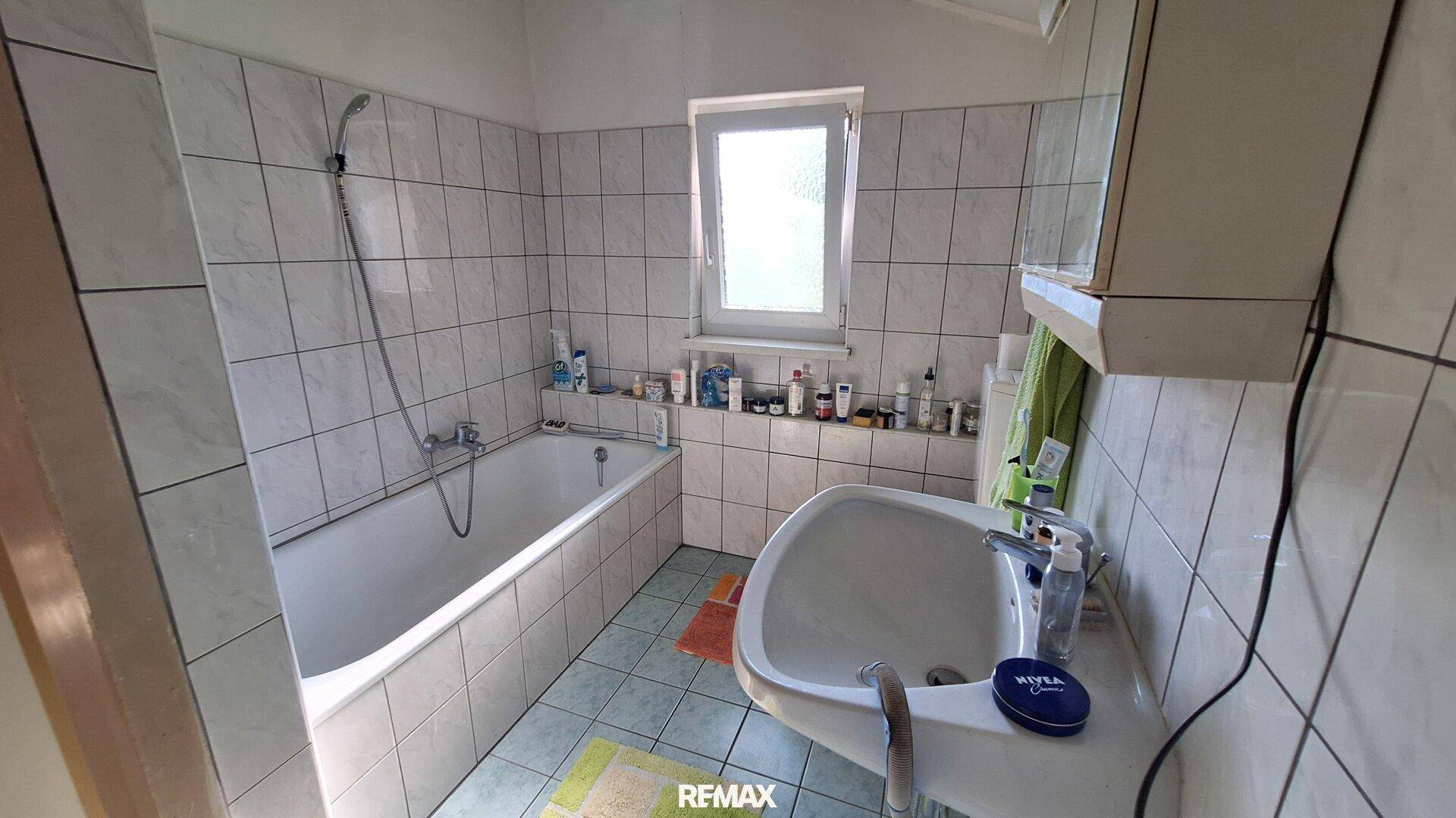 Helles Badezimmer mit Badewanne, Duschfunktion, Waschbecken und einem Fenster für natürliche Belüftung.