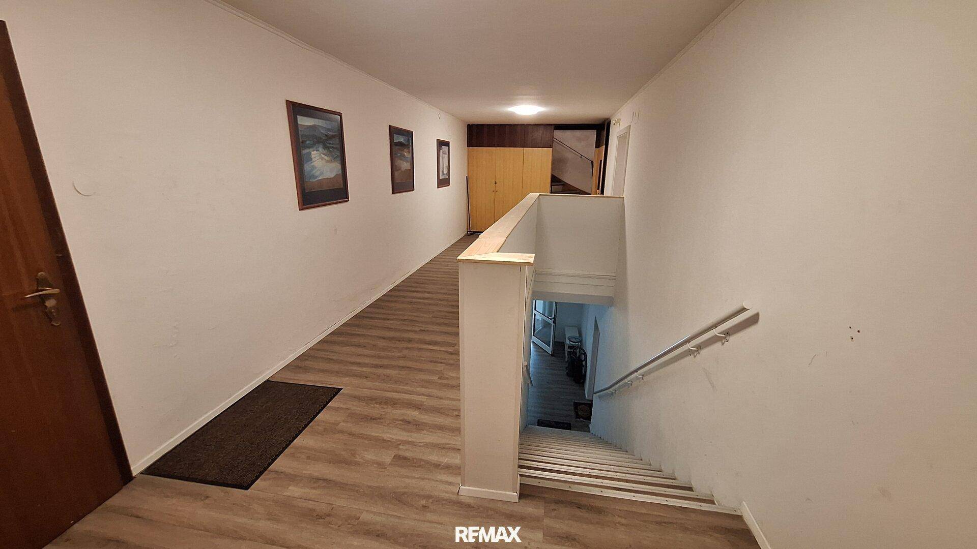 Langer Flur mit Holzfußboden und Treppe, die in ein unteres Stockwerk führt.