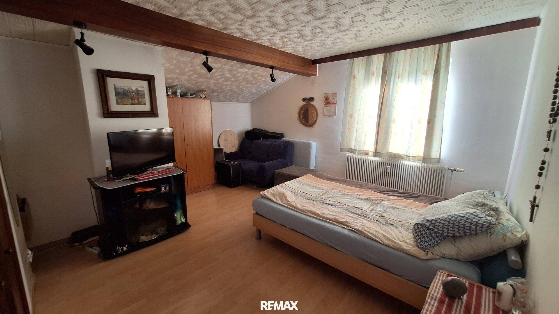 Schlafzimmer im Dachgeschoss mit Einzelbett, Fernseher, Holzbalken und schrägen Decken.
