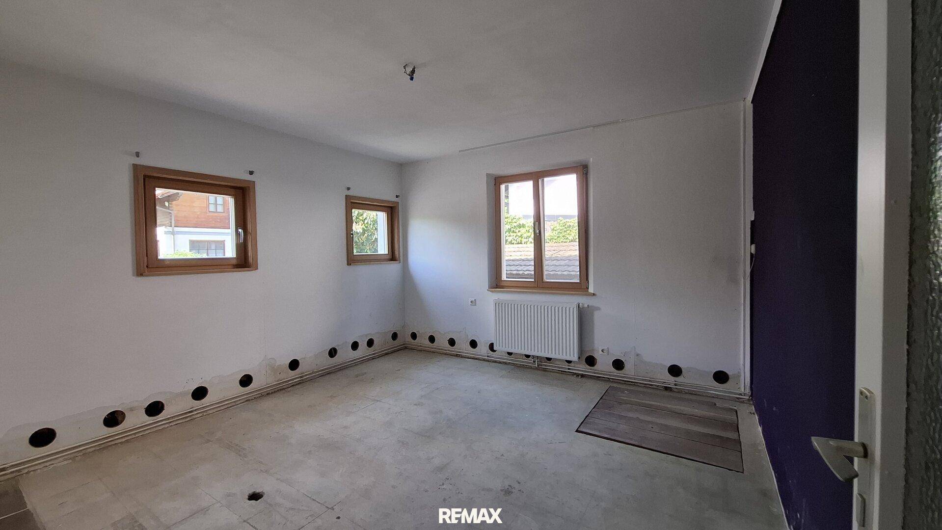 Unmöbliertes Zimmer mit hellen Wänden, Holzfenstern und Blick ins Grüne.