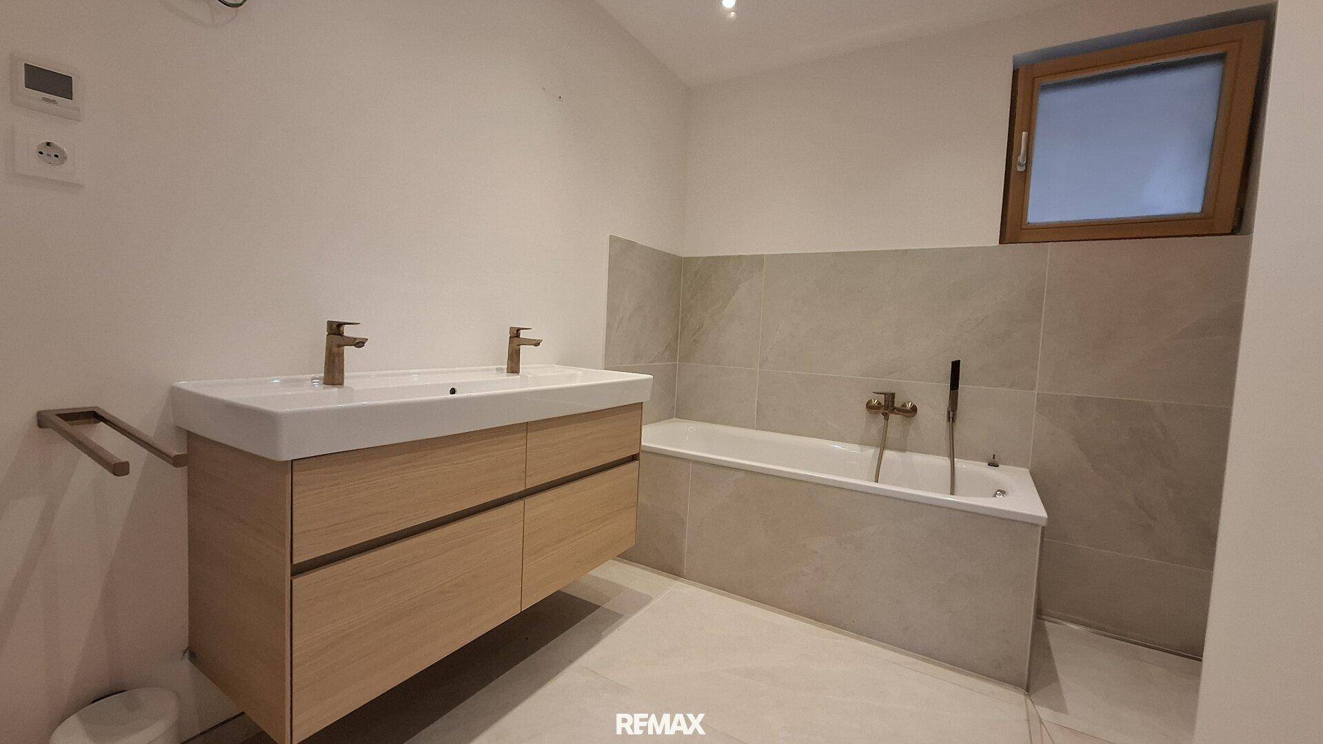 Modernes Badezimmer mit Doppelwaschbecken, Badewanne und großen Fliesen.
