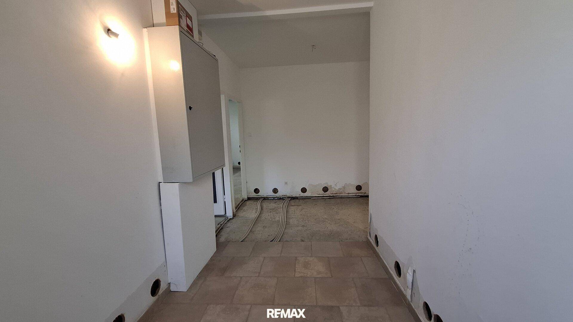 Heller Flur mit Fliesenboden und sichtbaren Installationen, bereit für den Ausbau.