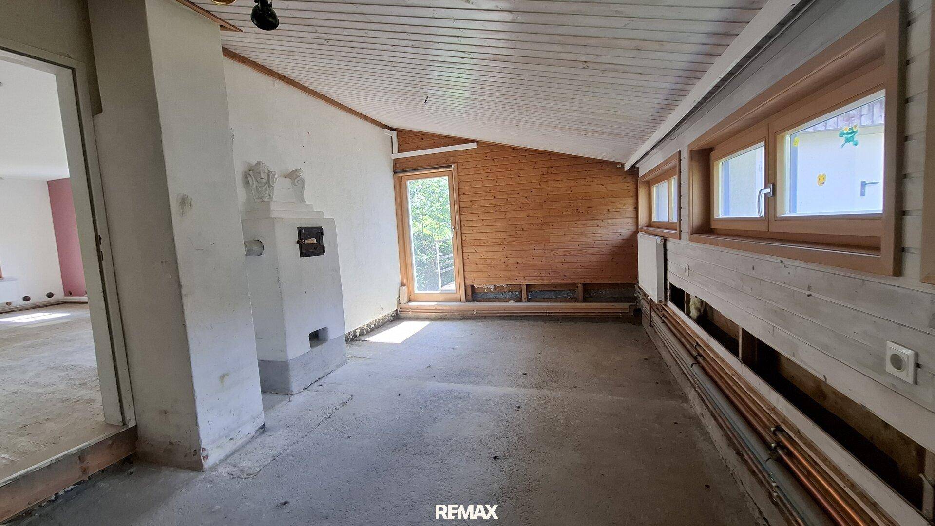 Dachgeschossraum mit Holzverkleidung, Kachelofen und schrägen Decken, bereit für Renovierung.