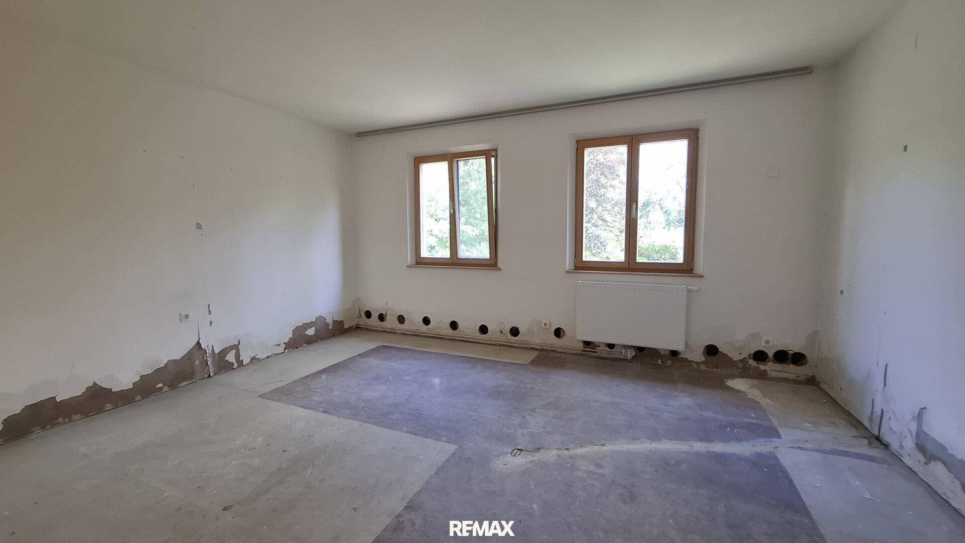 Unmöbliertes Zimmer mit Renovierungsbedarf, hellen Fenstern und Blick ins Grüne.