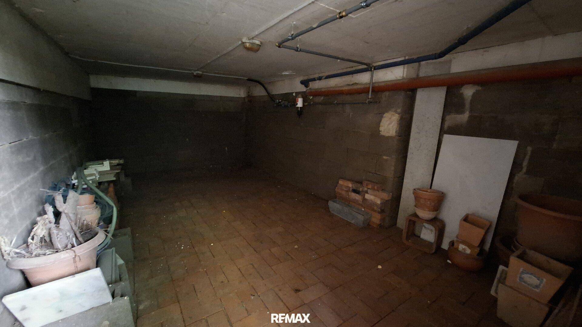 Unausgebauter Kellerraum mit Ziegelboden und sichtbaren Leitungen, ideal als Stauraum.