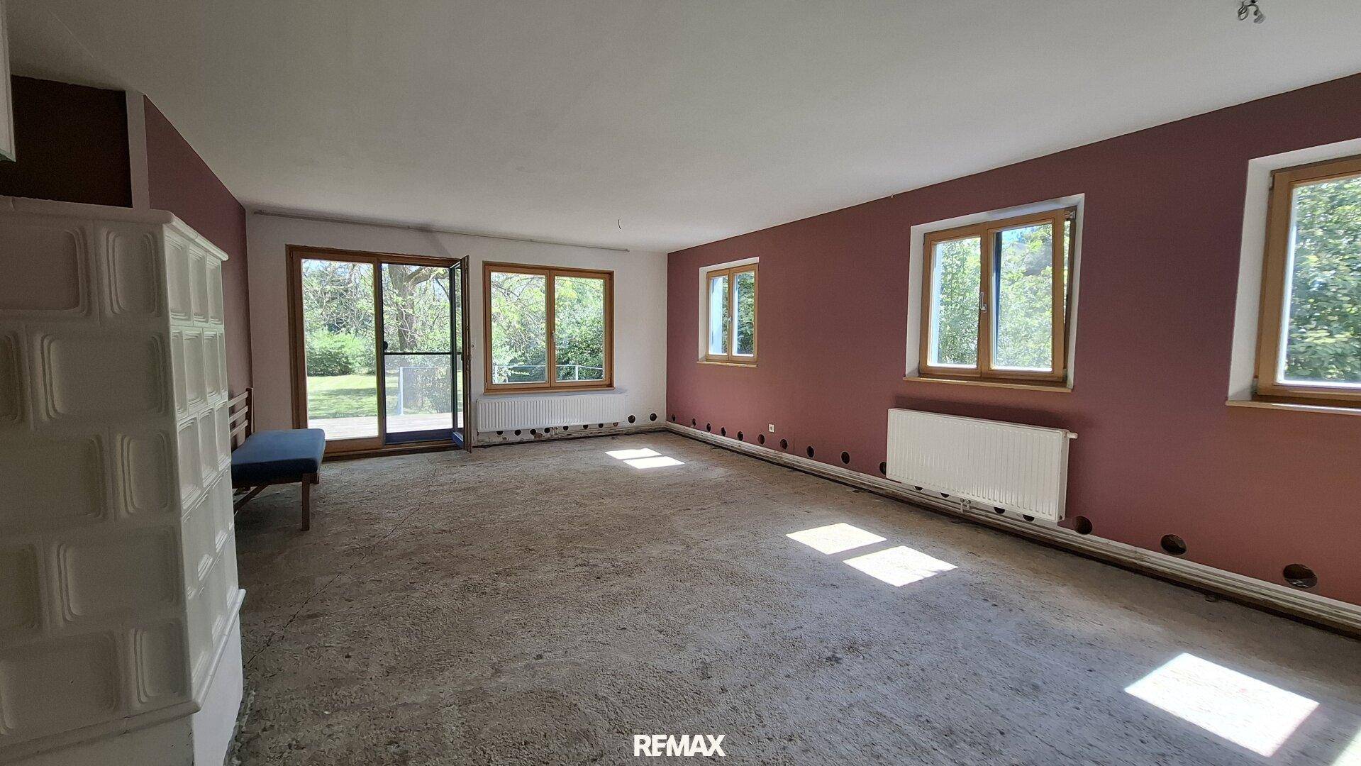 Geräumiger, unmöblierter Wohnbereich mit Terrakotta-Kachelofen und Zugang zur Terrasse.