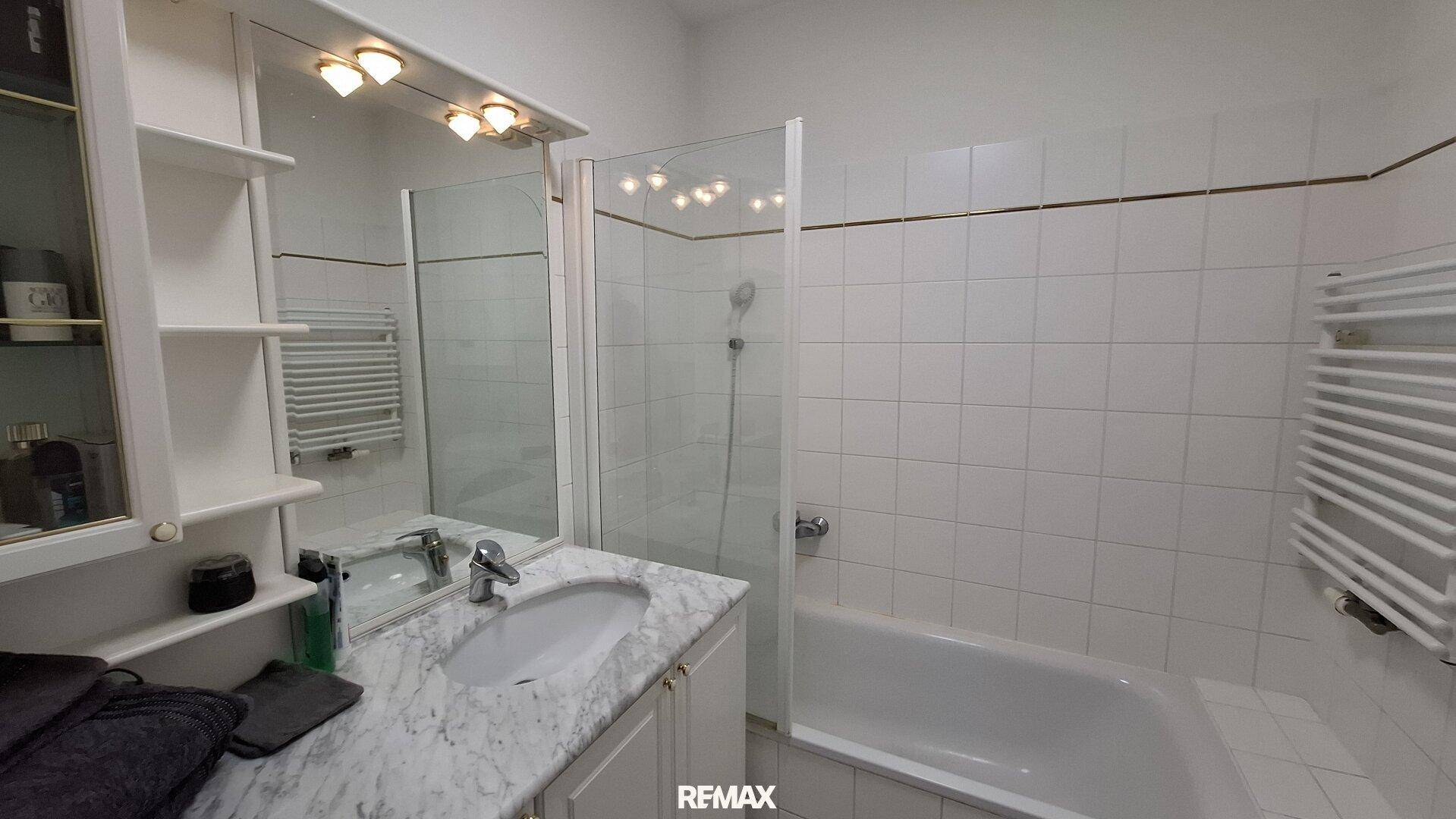 Helles Badezimmer mit Badewanne, Duschbereich, Einzelwaschbecken und beheiztem Handtuchhalter.