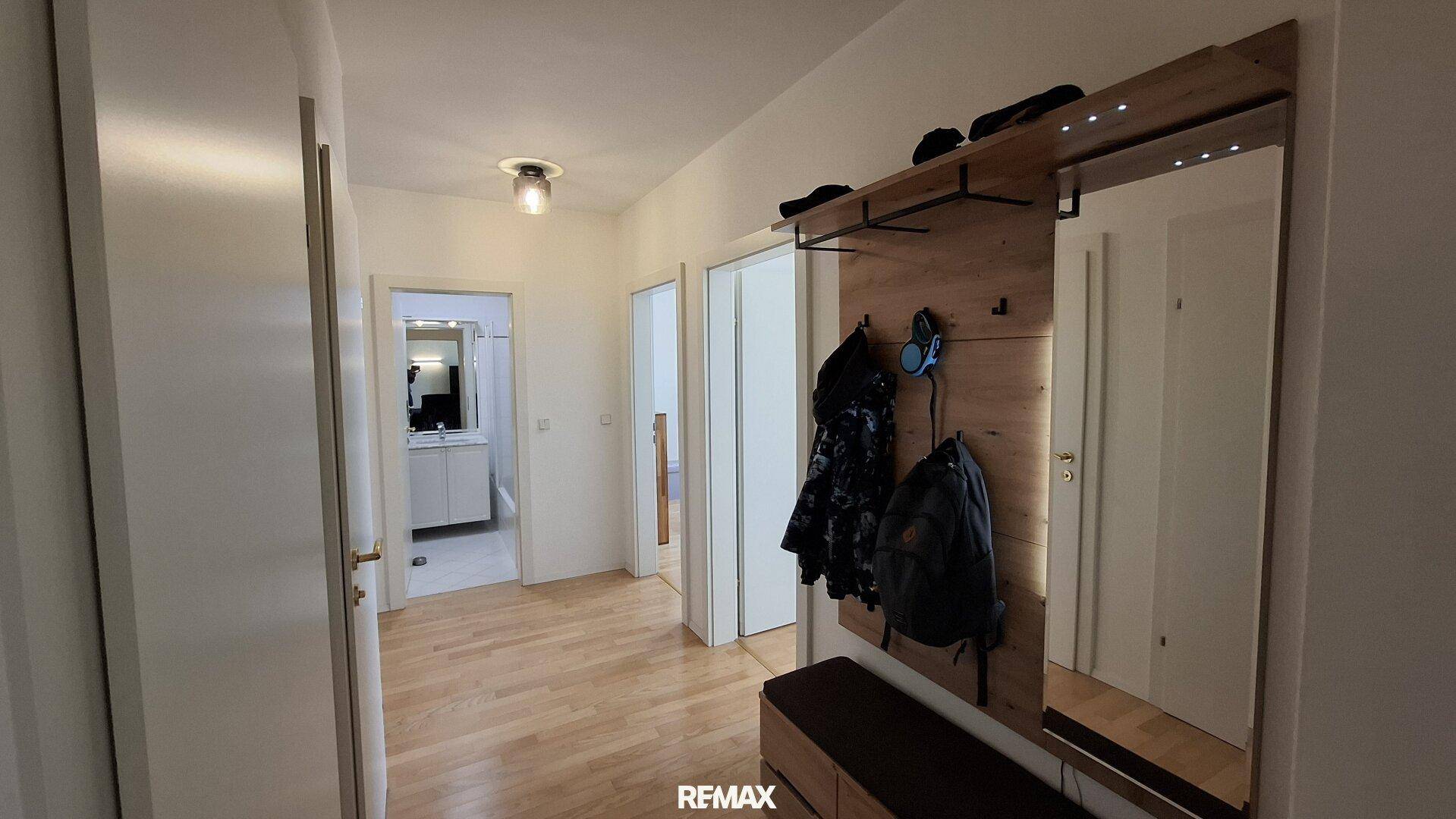 Heller Flur mit Garderobe, großem Spiegel und Holzfußboden, der zu weiteren Räumen führt.