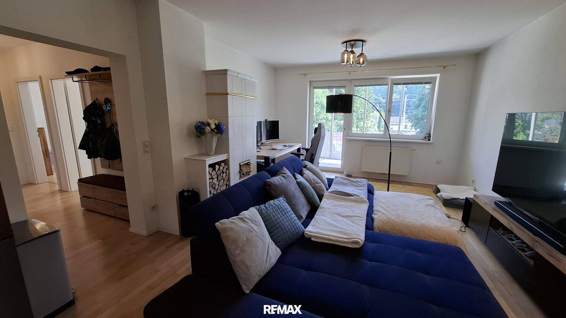 Gemütliches Wohnzimmer mit Sofa, Arbeitsbereich und großem Fenster mit Blick ins Grüne.