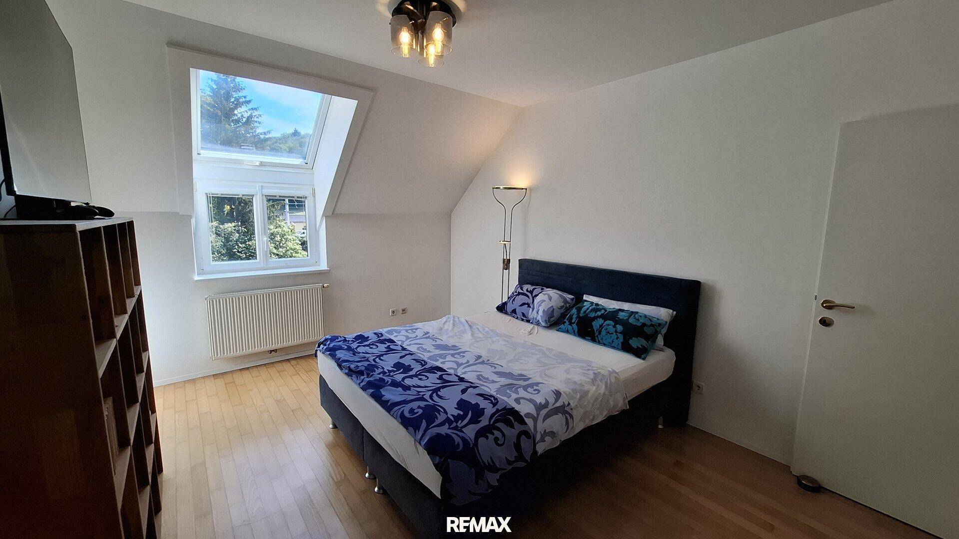 Schlafzimmer mit Doppelbett, Holzfußboden und Dachfenster unter einer Dachschräge für viel Licht.