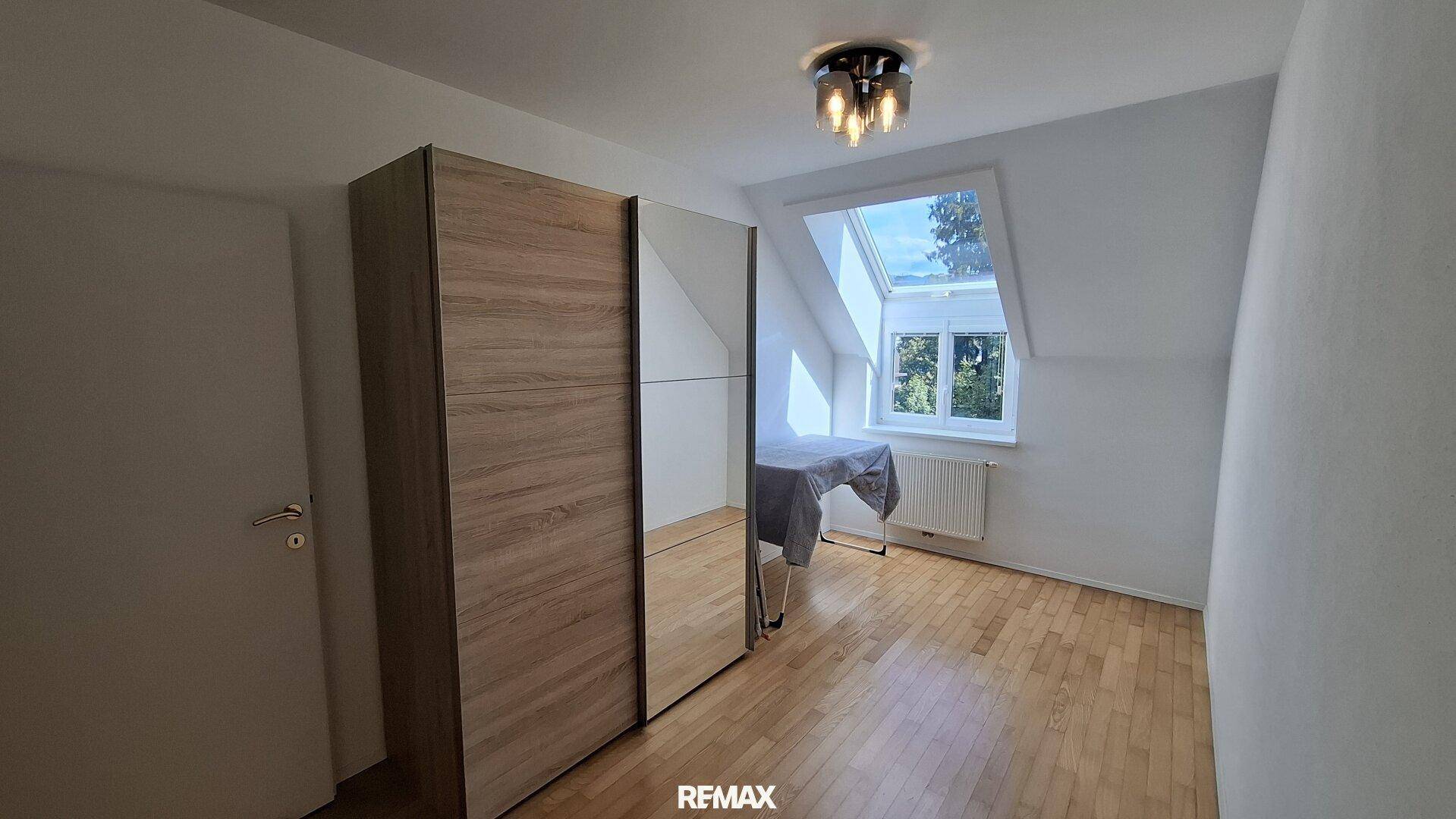 Helles Zimmer mit großem Kleiderschrank, Holzfußboden und Dachfenster unter Dachschräge.