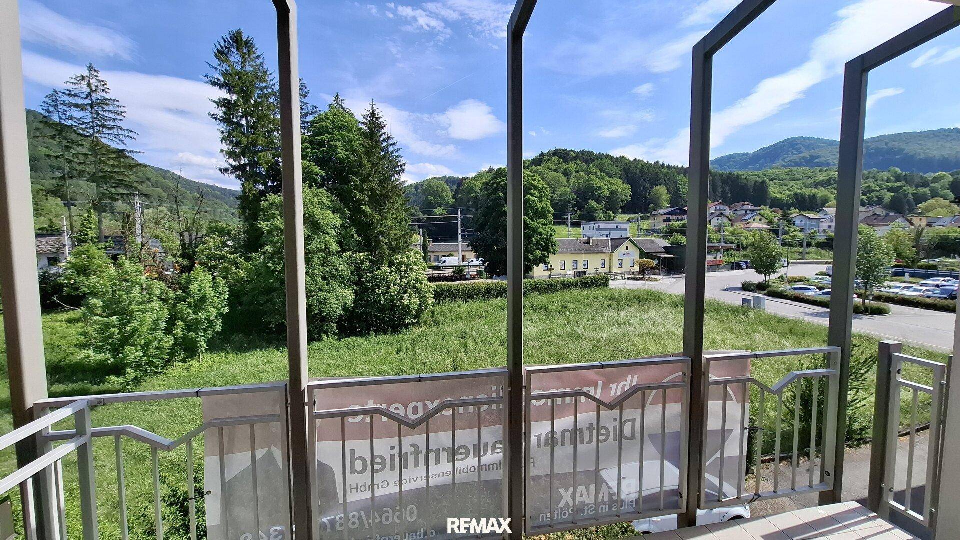 Weitläufiger Ausblick vom Balkon auf grüne Landschaft, Berge und entfernte Häuser unter blauem Himmel.