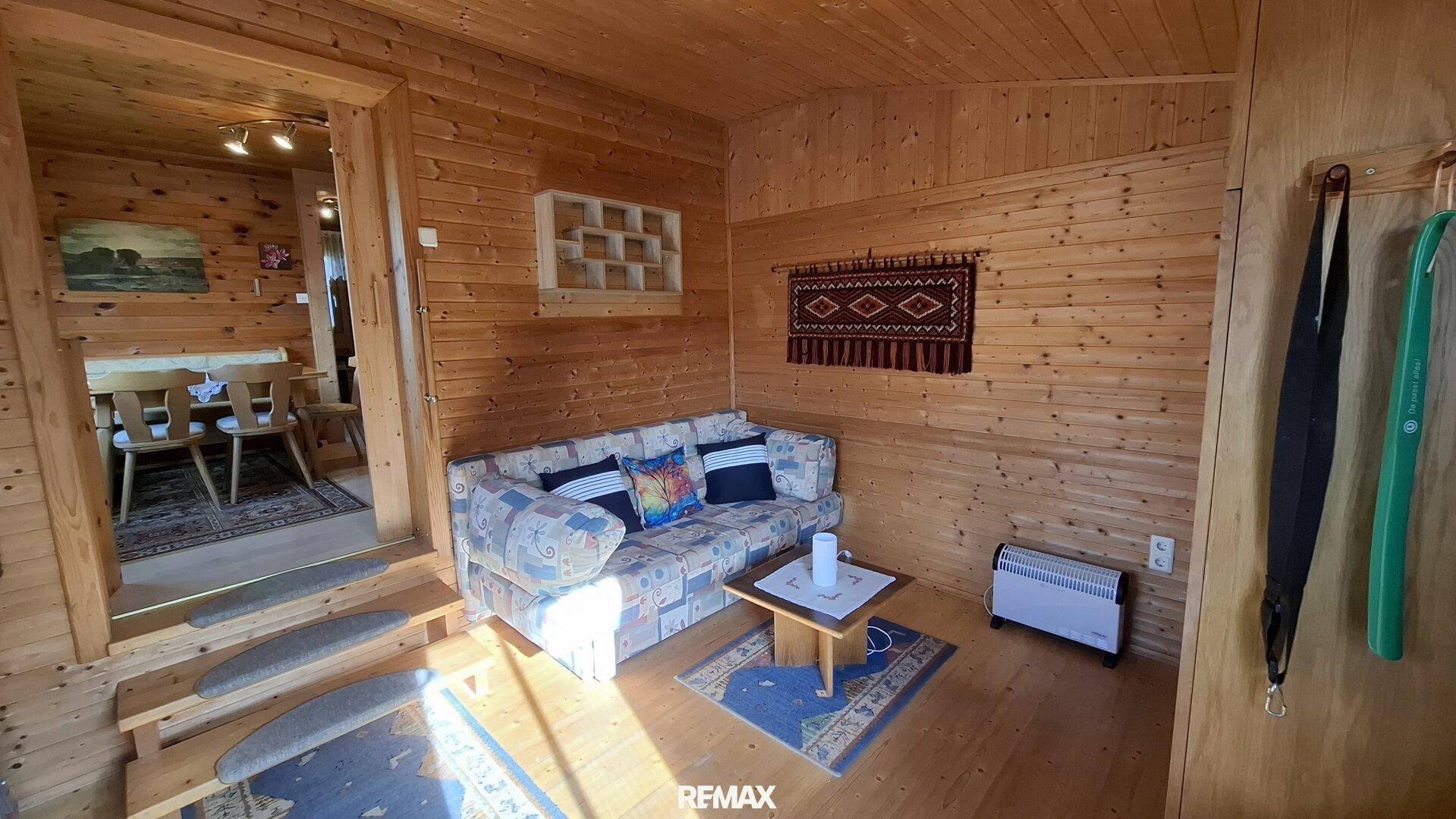 Rustikales Wohnzimmer mit Holztäfelung, Sofa und Zugang zum Essbereich.
