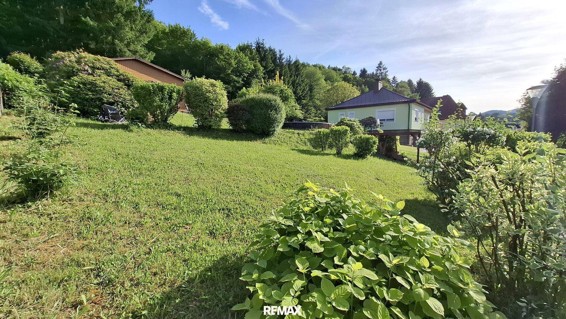 Weitläufiger Garten mit Rasenfläche, Sträuchern und Blick auf die umliegende Natur.