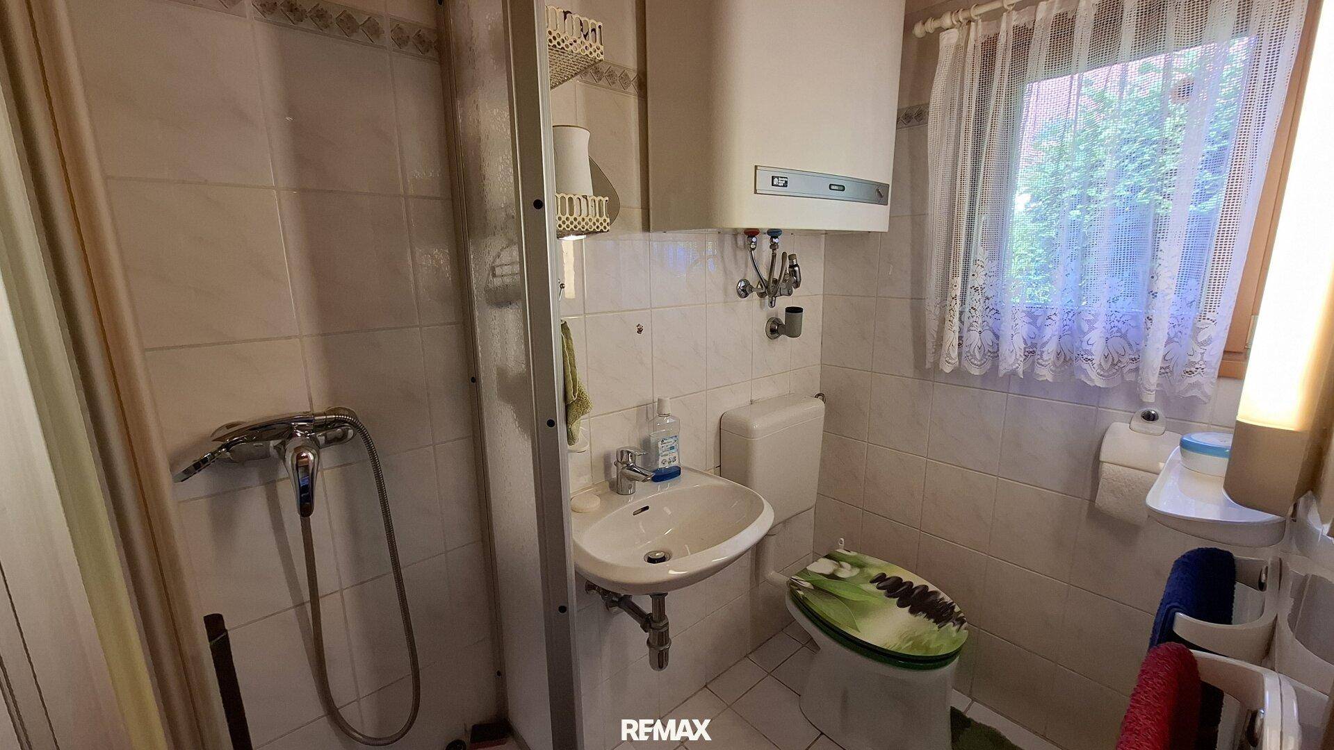 Kleines Badezimmer mit Fliesen, Dusche, Waschbecken und Fenster.