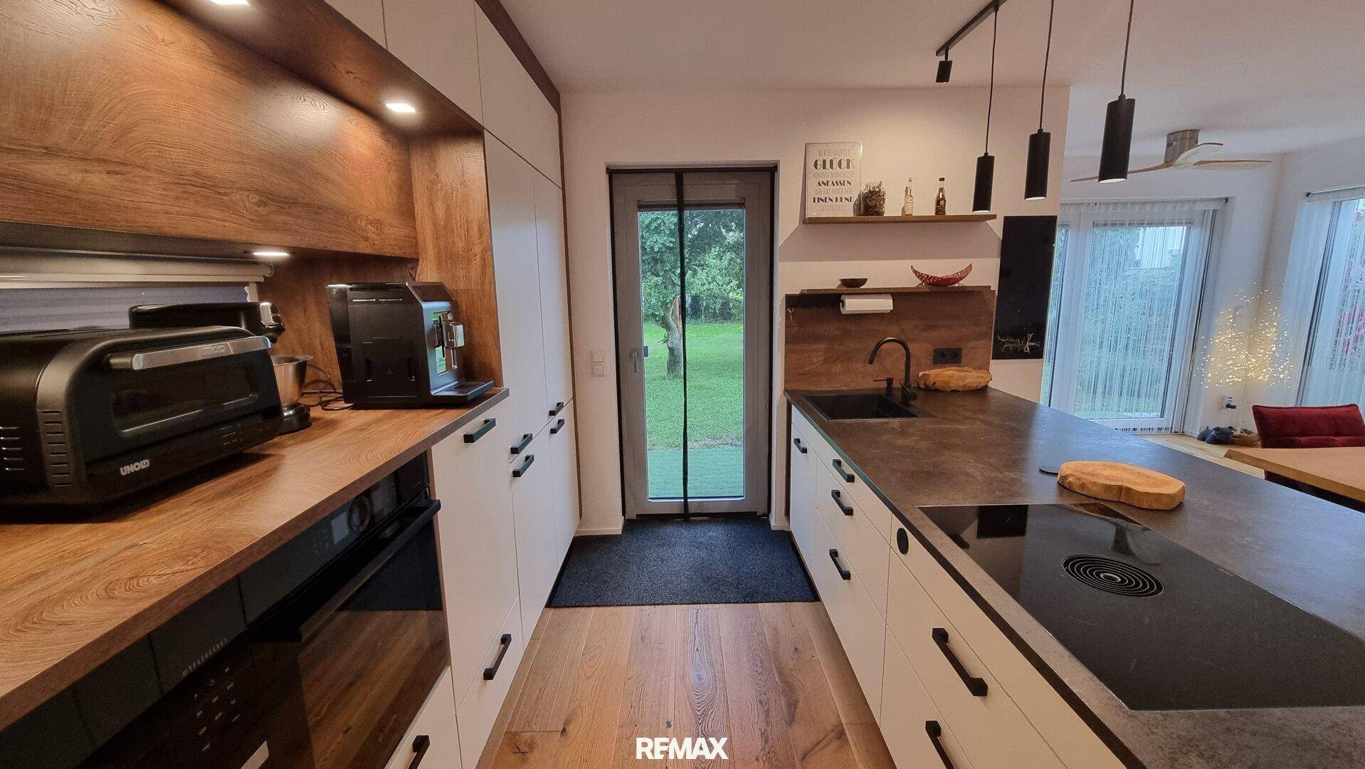 Moderne Küche mit weiß-holzfarbenen Schränken, Kochinsel und direktem Zugang zum Garten.