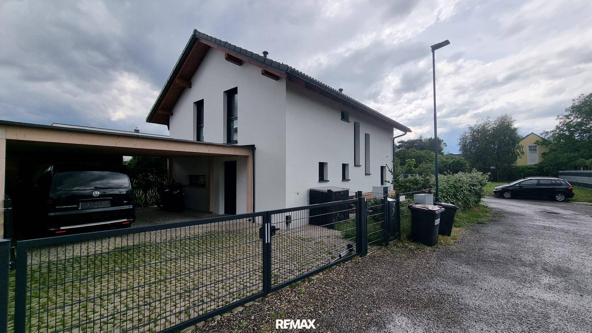Ansicht des modernen Einfamilienhauses mit Carport und gepflasterter Zufahrt unter bewölktem Himmel.