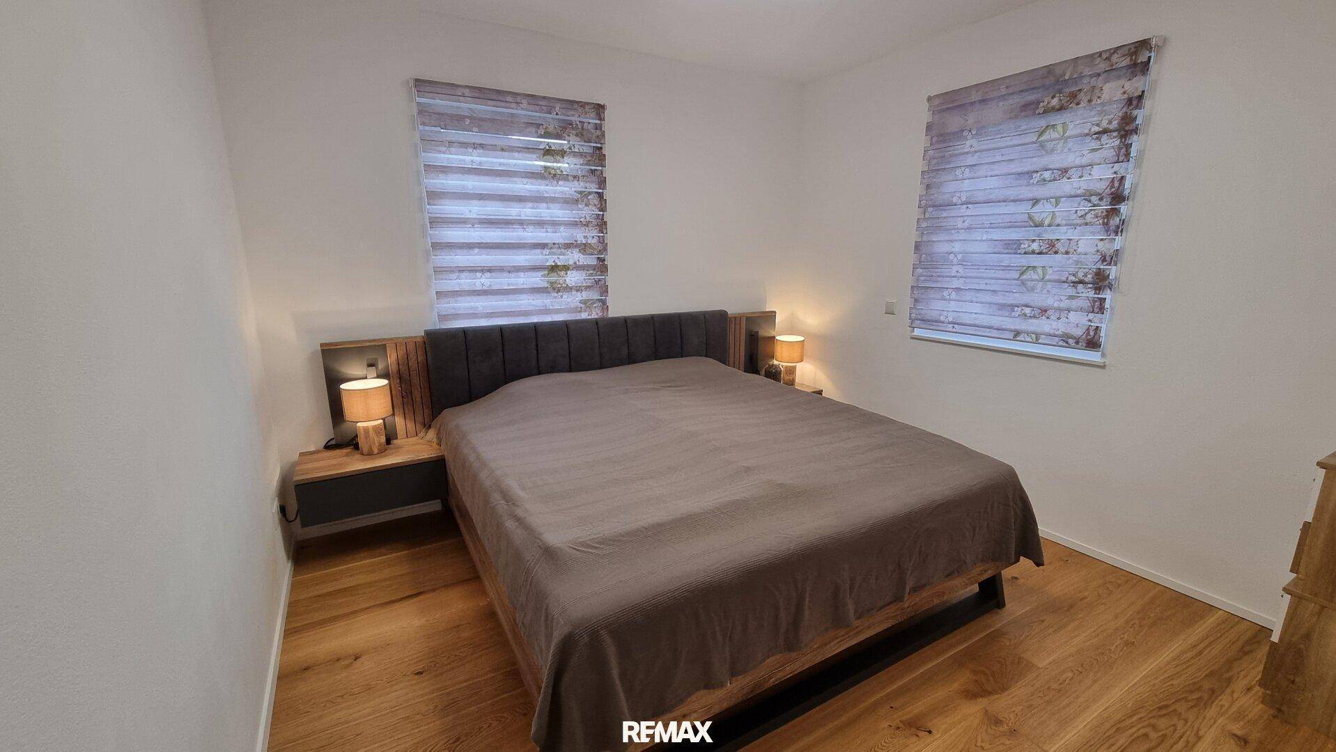 Schlafzimmer mit Doppelbett, Nachttischen und zwei Fenstern für natürliches Licht.