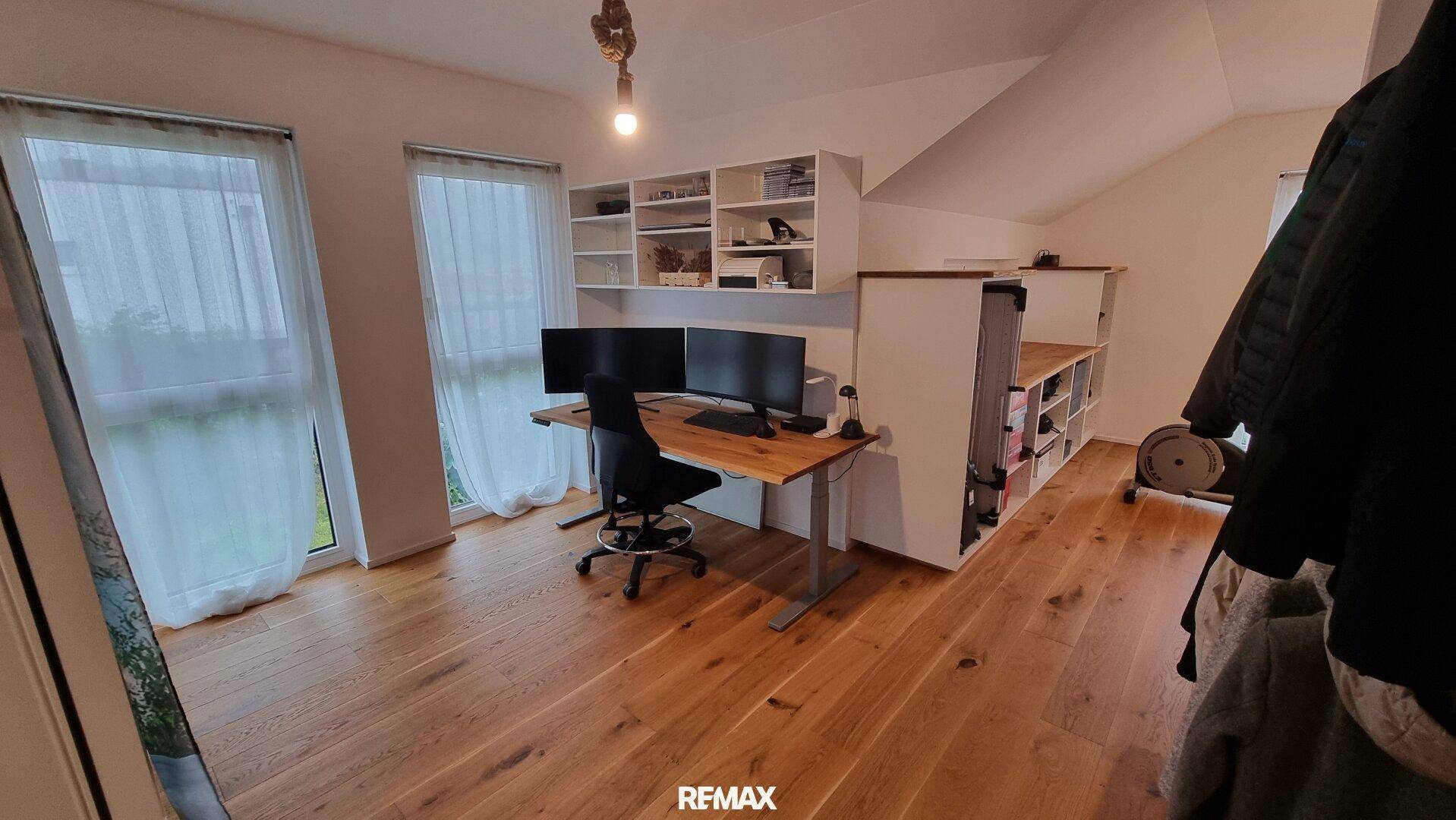 Helles Heimbüro mit zwei Monitoren, Schreibtisch und praktischen Regalsystemen unter der Dachschräge.