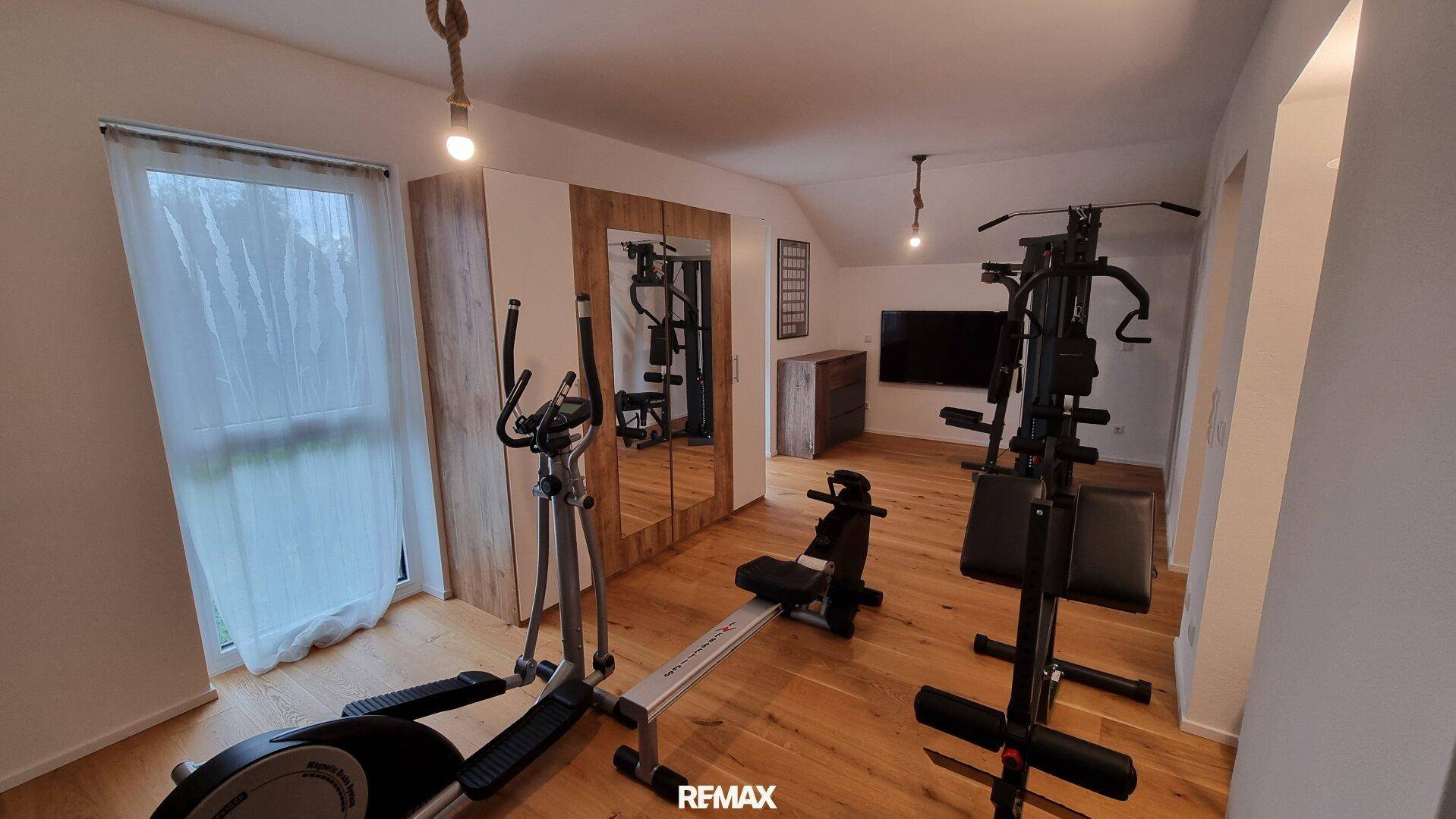 Privater Fitnessraum mit verschiedenen Trainingsgeräten und Holzboden unter der Dachschräge.