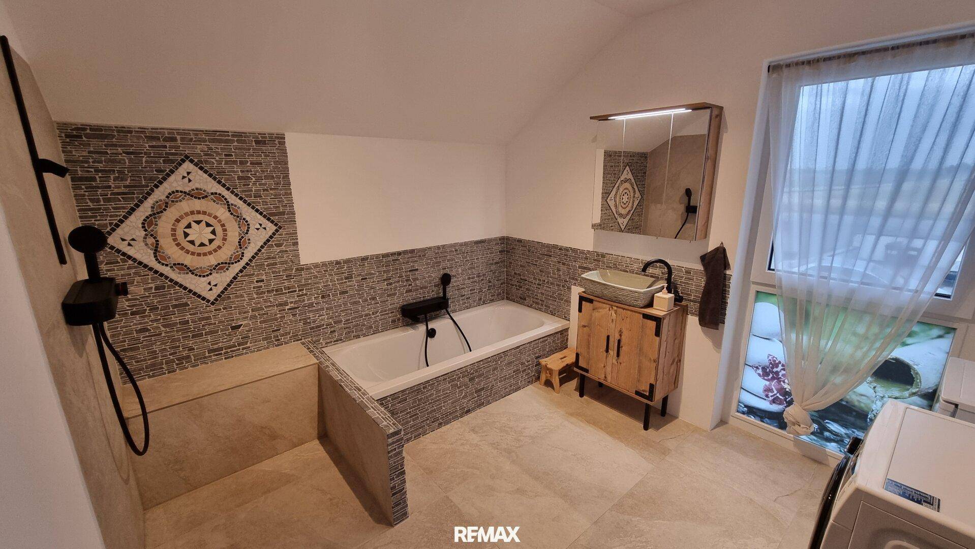 Geräumiges Badezimmer mit Badewanne, Duschbereich, Fenster und dekorativen Fliesen.