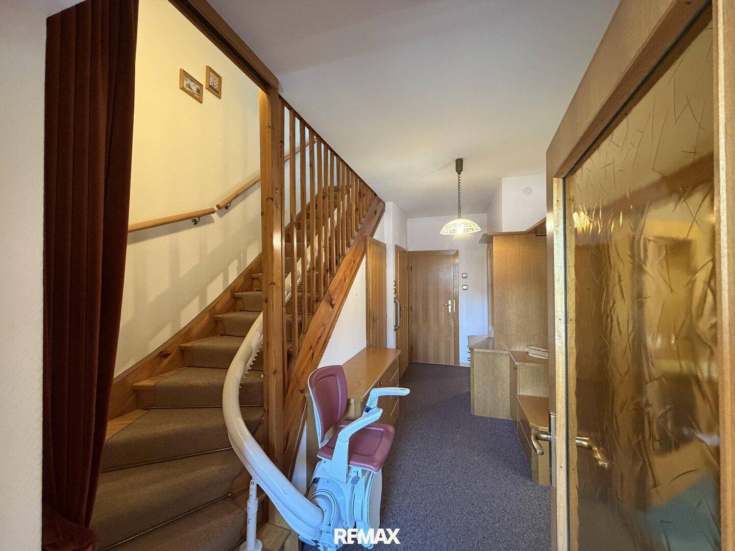 Flur mit Holztreppe, Teppichboden und installiertem Treppenlift für Barrierefreiheit.