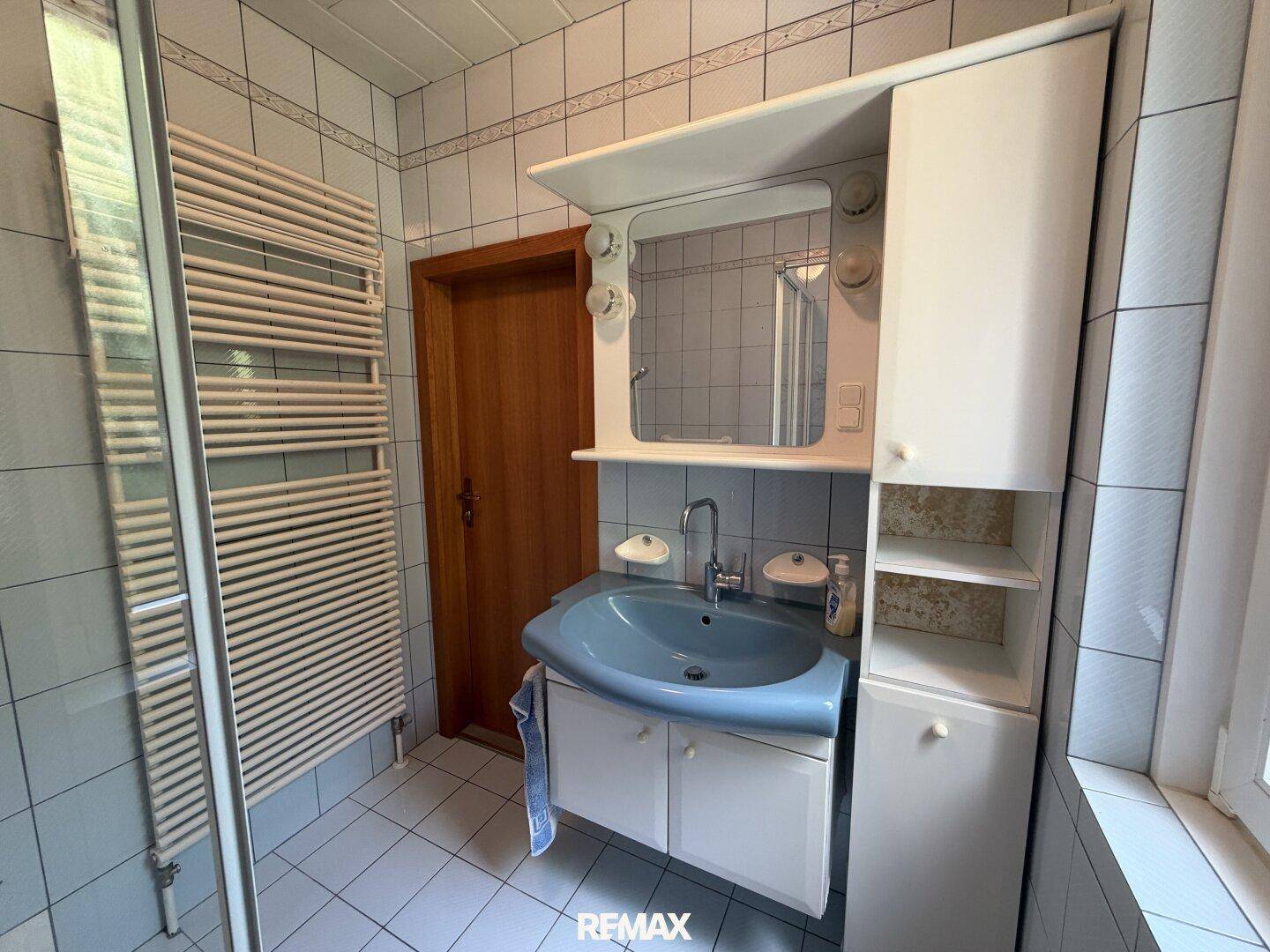 Badezimmer mit hellblauer Waschtisch, Spiegelschrank und Handtuchheizkörper.