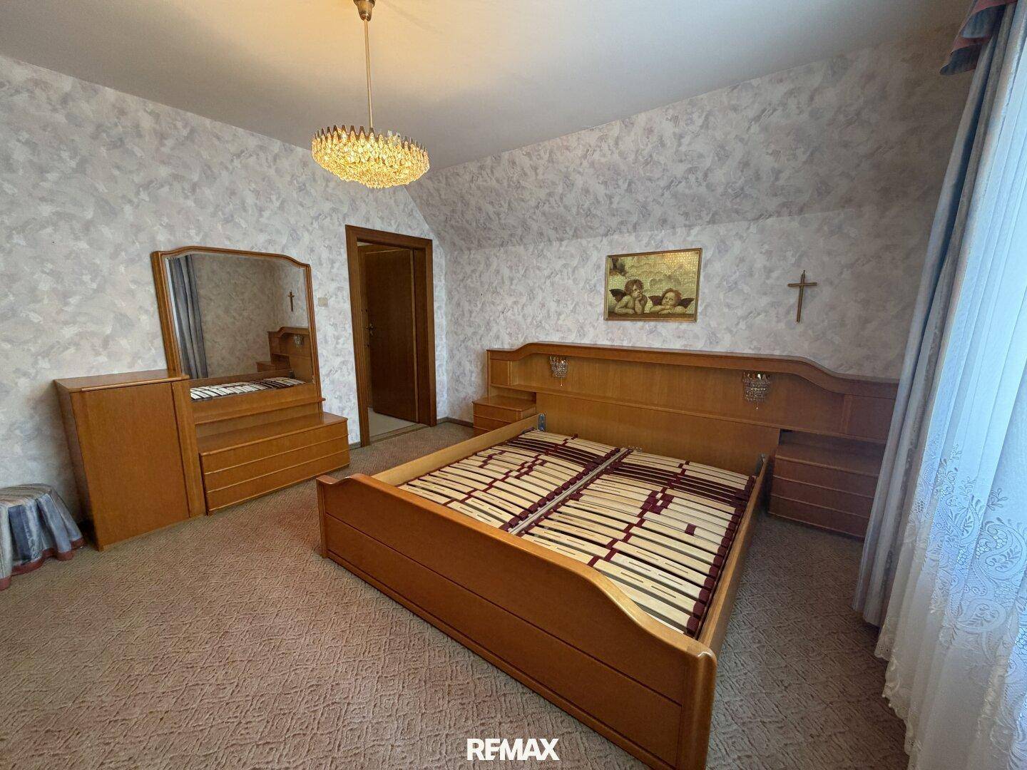 Schlafzimmer mit Doppelbett, Holzmöbeln und Teppichboden unter Dachschräge.