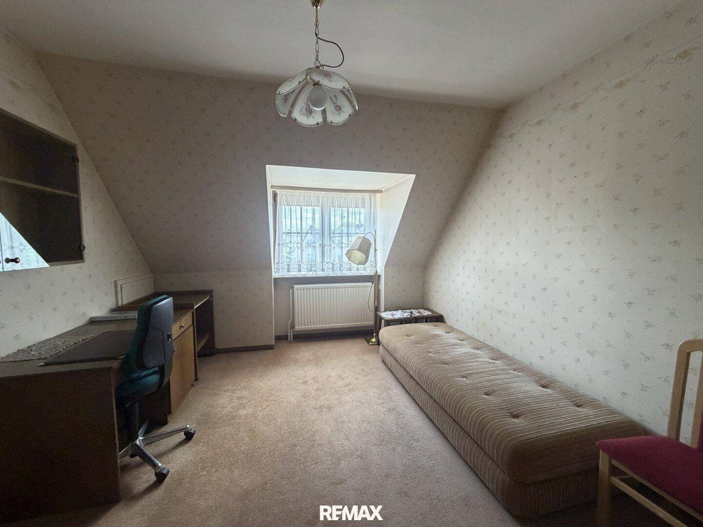 Helles Schlafzimmer oder Arbeitszimmer mit Einzelbett, Schreibtisch und Dachschräge.