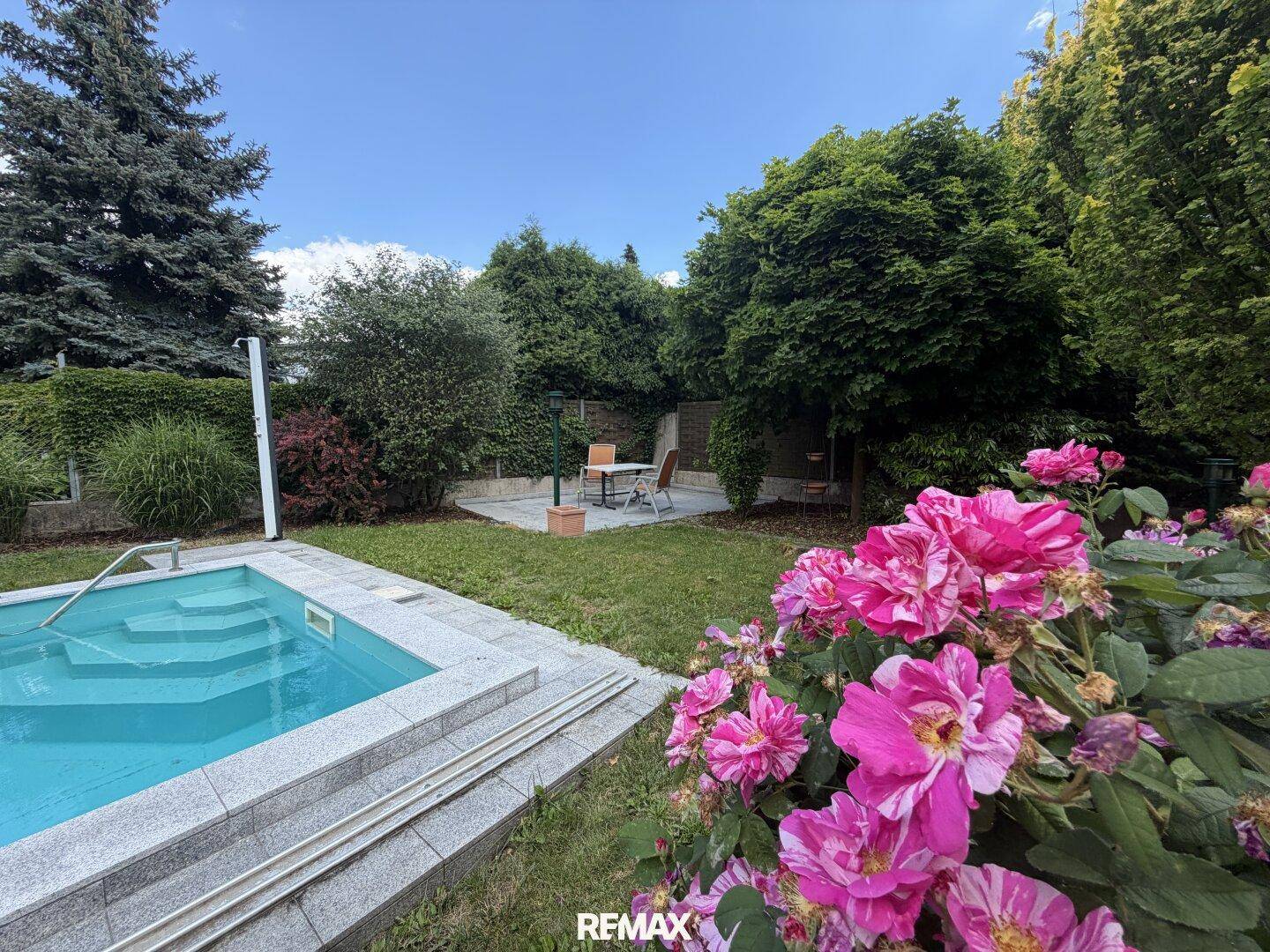 Gepflegter Gartenbereich mit Pool, blühenden Rosen und Sitzgelegenheit.