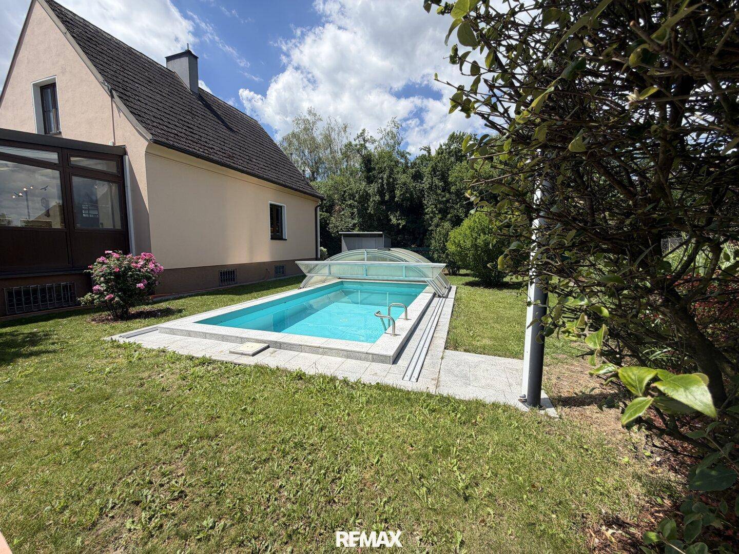 Seitenansicht des Hauses mit Pool im Garten unter blauem Himmel.