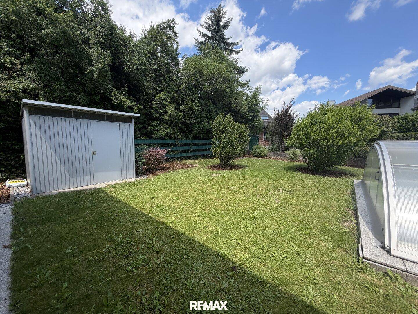 Weitläufige Rasenfläche mit einem praktischen Gartenschuppen und Blick auf den Poolbereich.