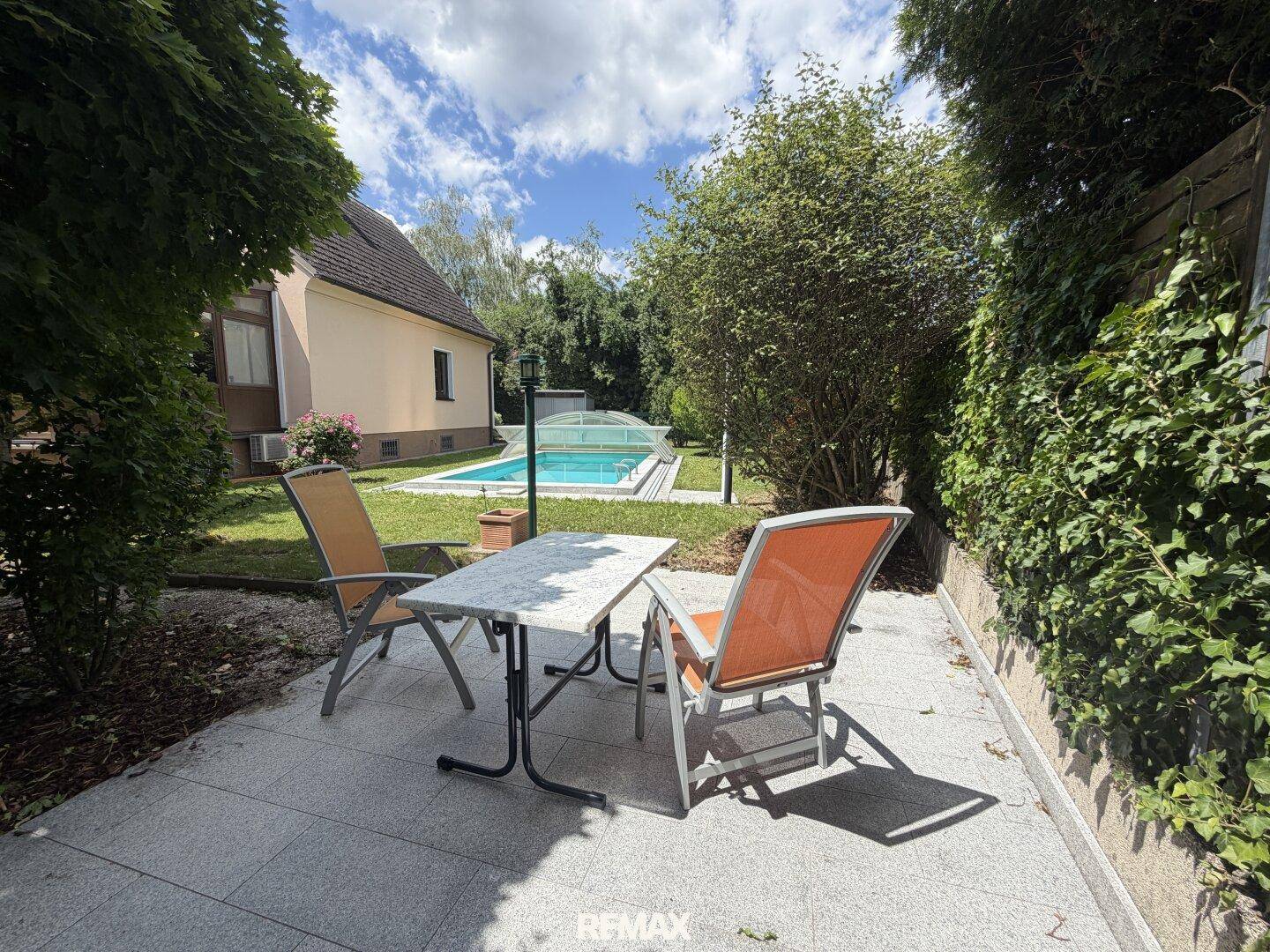 Gemütliche Terrasse mit Gartenmöbeln und Blick auf den Pool, umgeben von üppigem Grün.