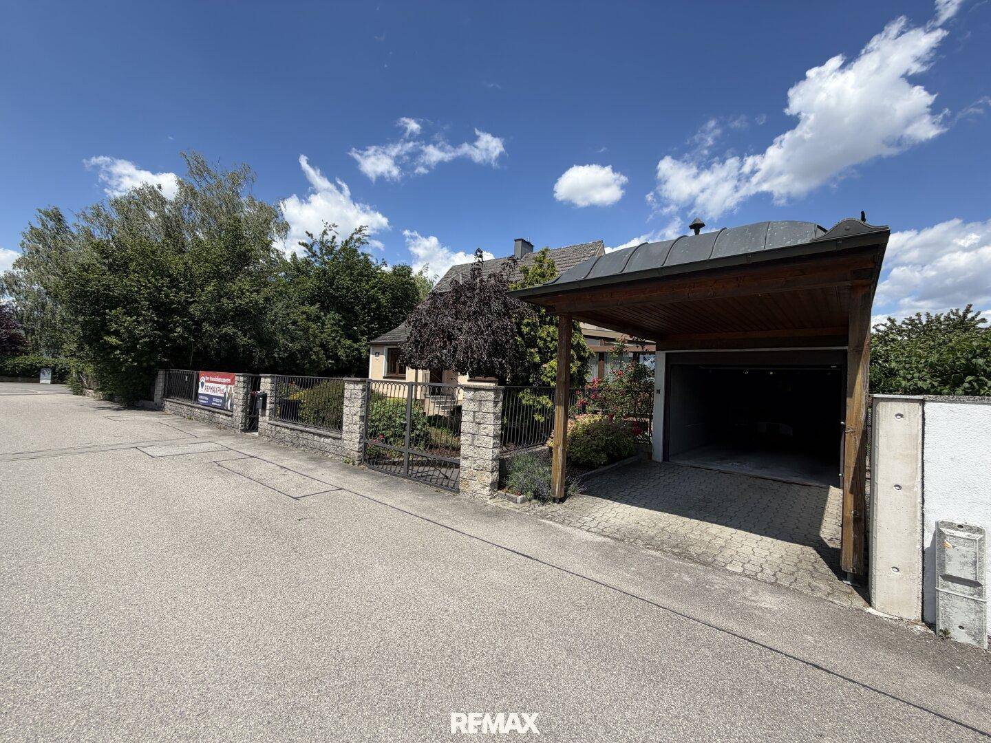 Zufahrt zum Grundstück mit Carport und Steinmauer an der Straße.