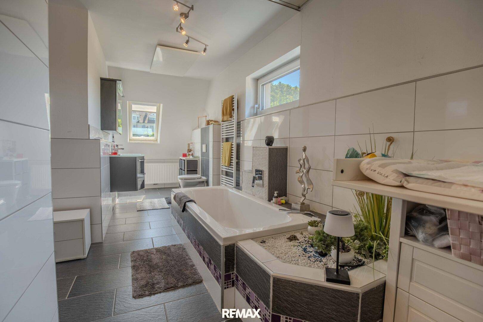 Geräumiges Badezimmer mit Badewanne, dunklen Bodenfliesen und zwei Fenstern für Tageslicht.