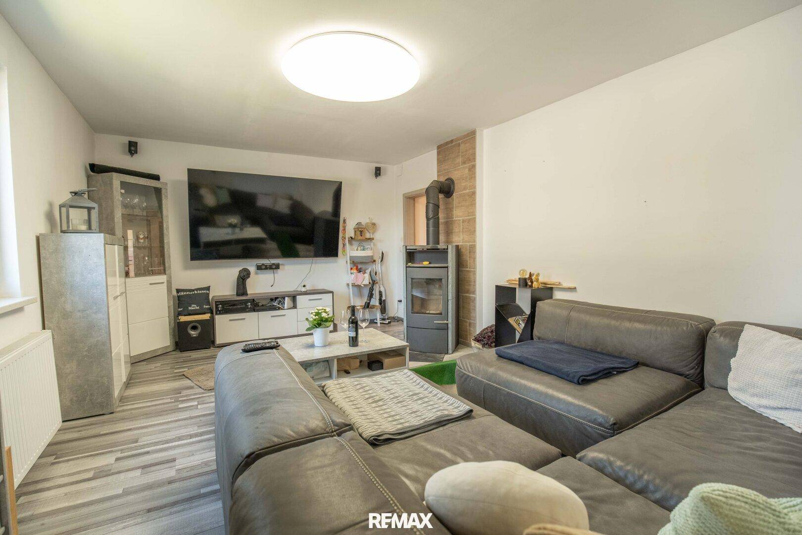 Gemütliches Wohnzimmer mit großem Sofa, Holzboden und einem modernen Holzofen.