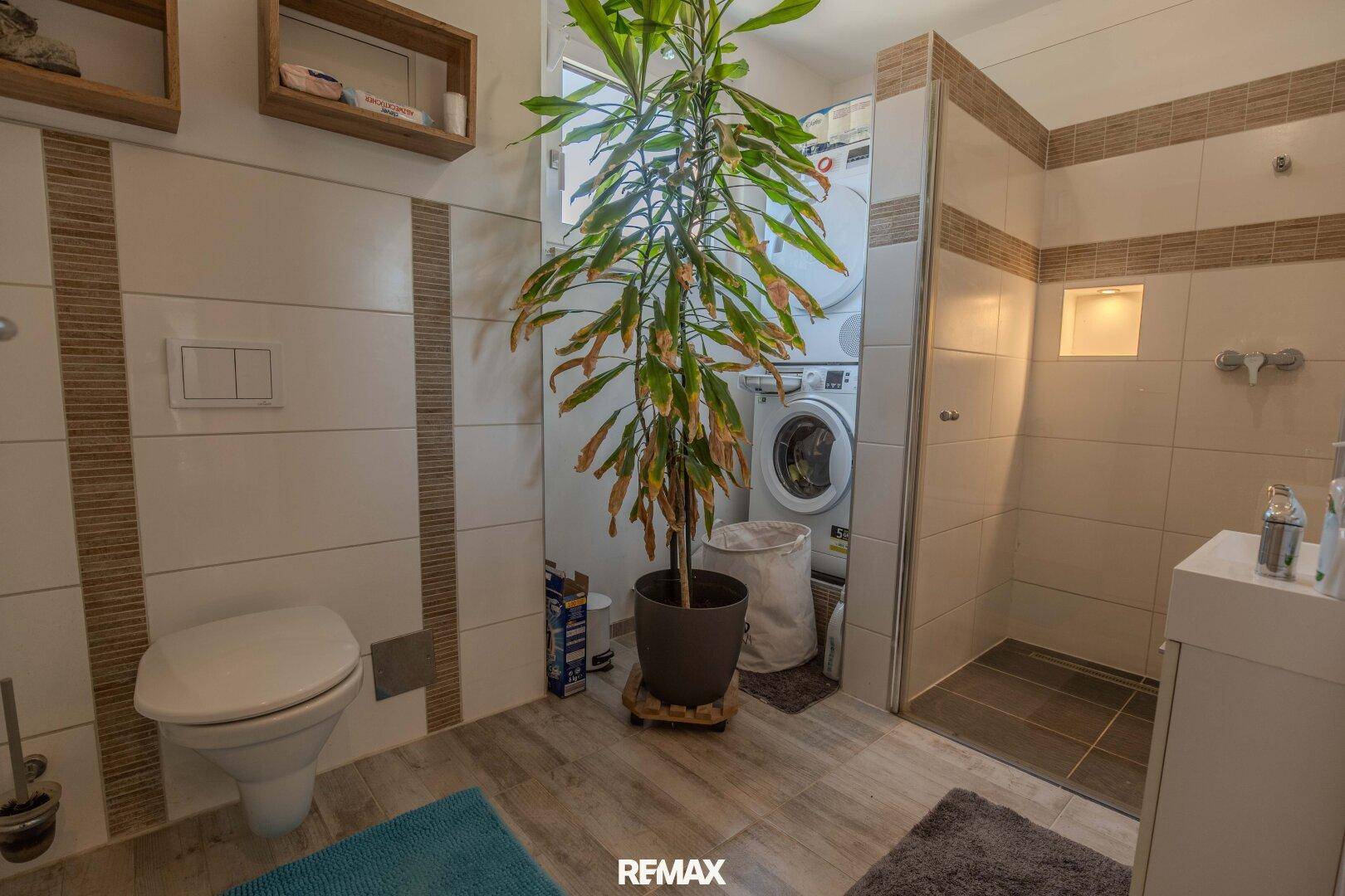 Badezimmer mit WC, Dusche und integrierter Waschmaschine und Trockner.