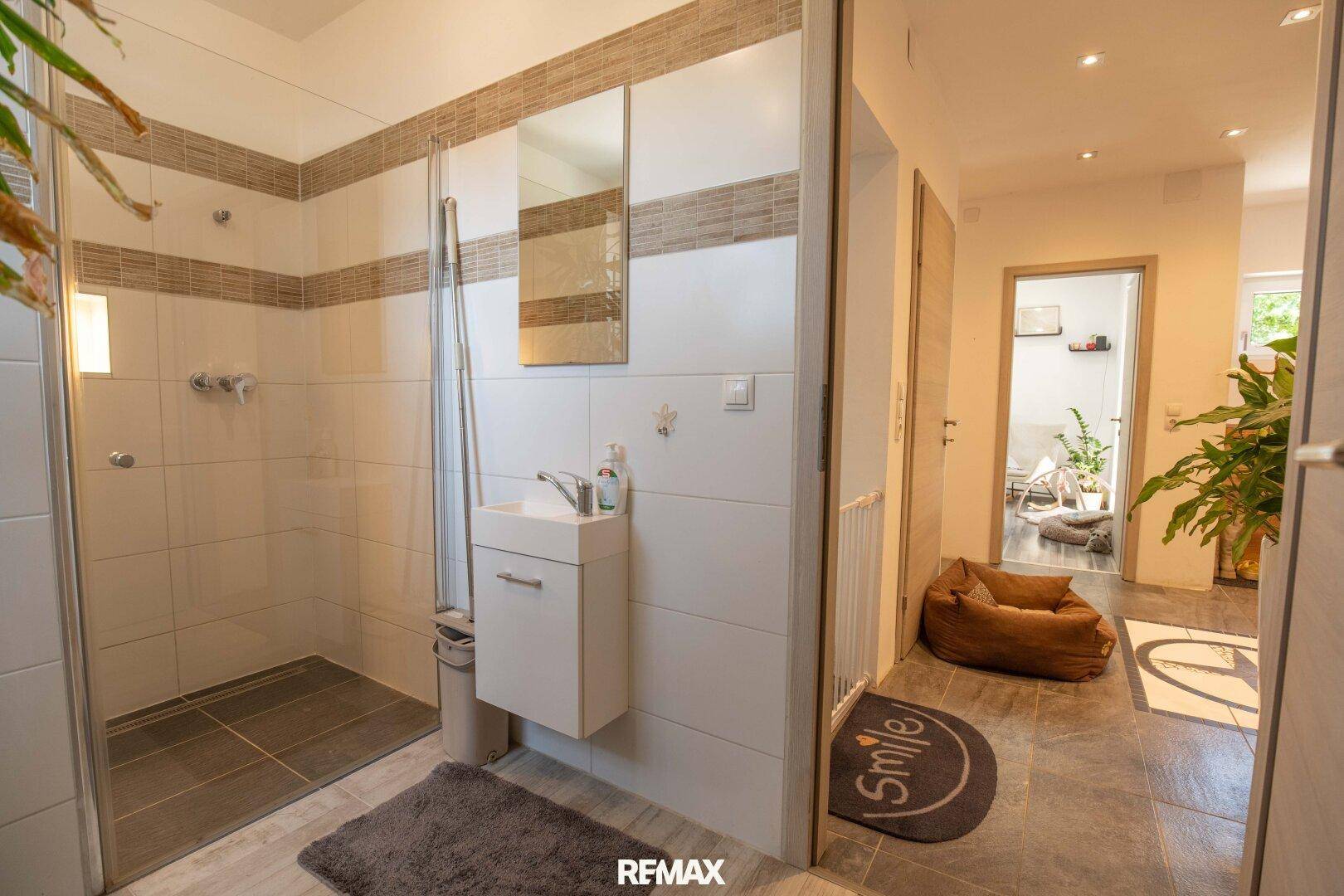 Modernes Badezimmer mit Duschbereich, kleinem Waschbecken und Spiegel.