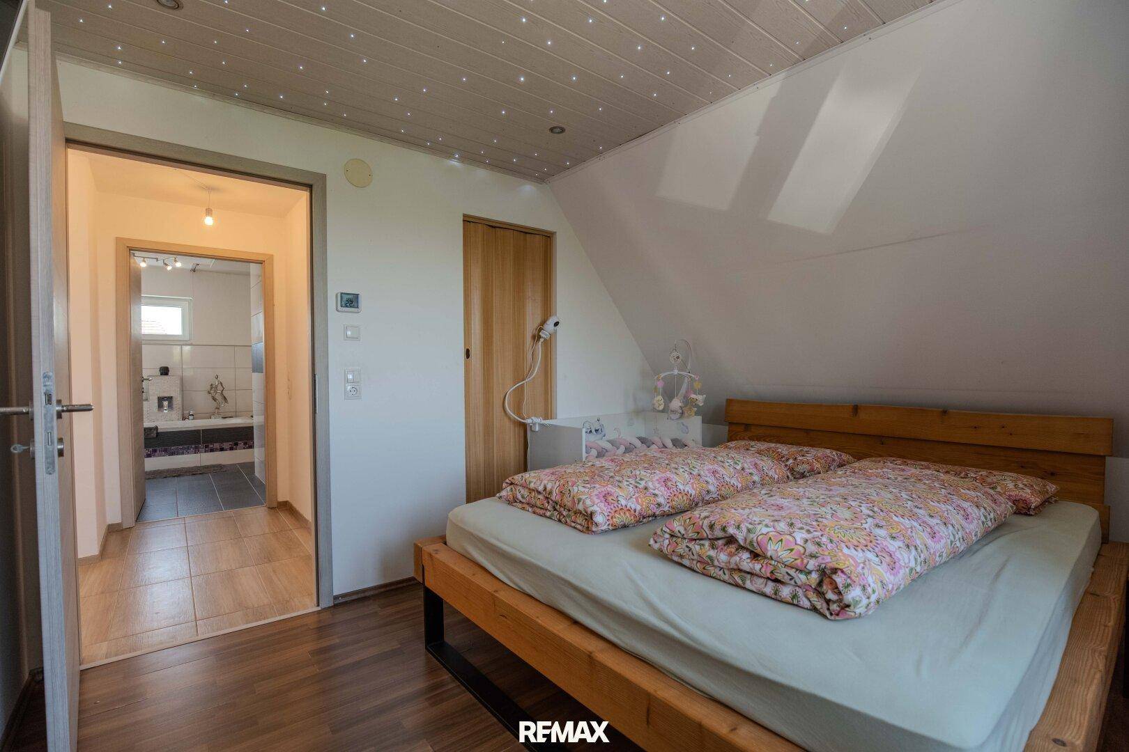 Schlafzimmer mit Holzbett, Dachschräge und direktem Zugang zum Badezimmer.
