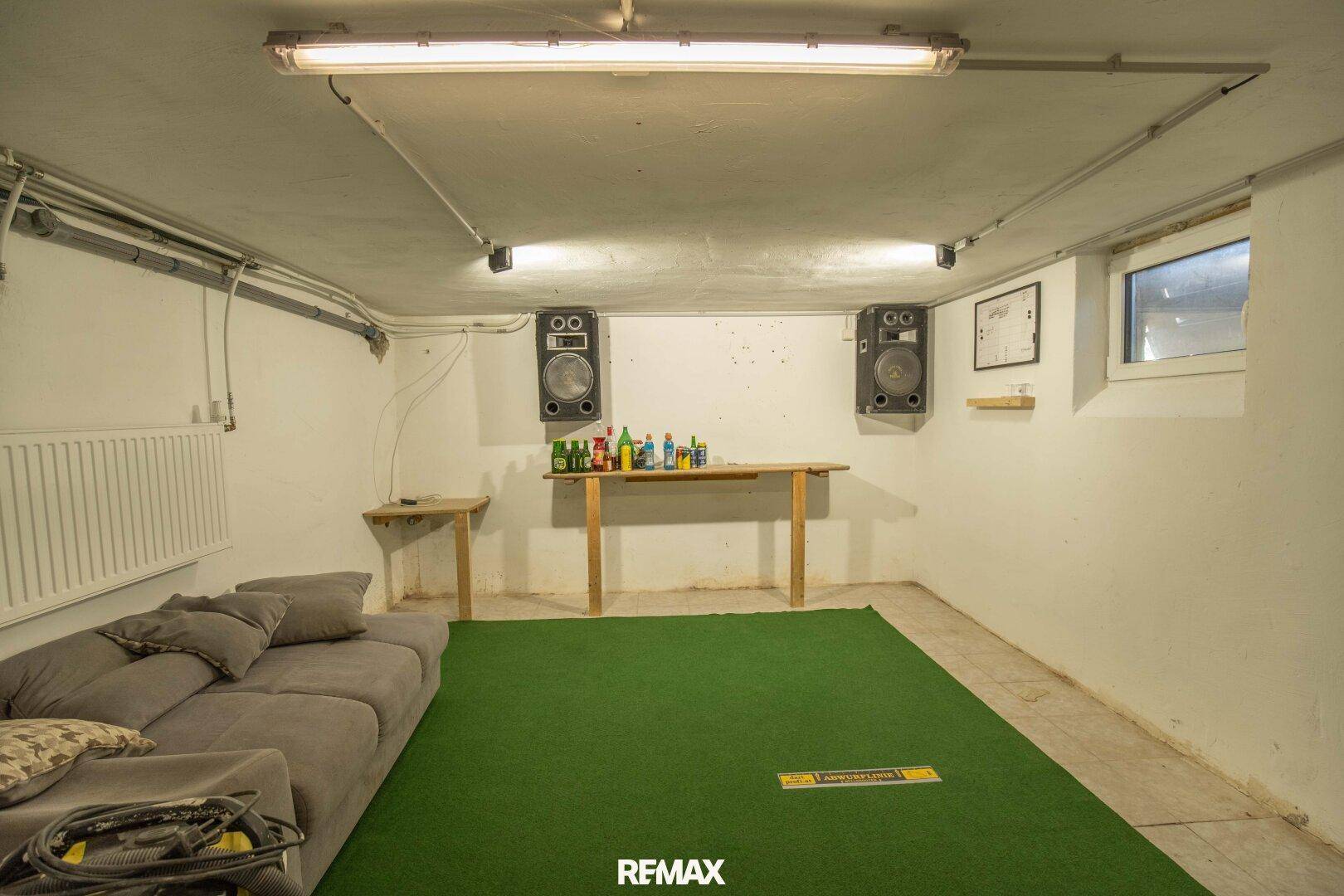 Hobbyraum im Keller mit Sofa, Teppichboden und Lautsprechern.