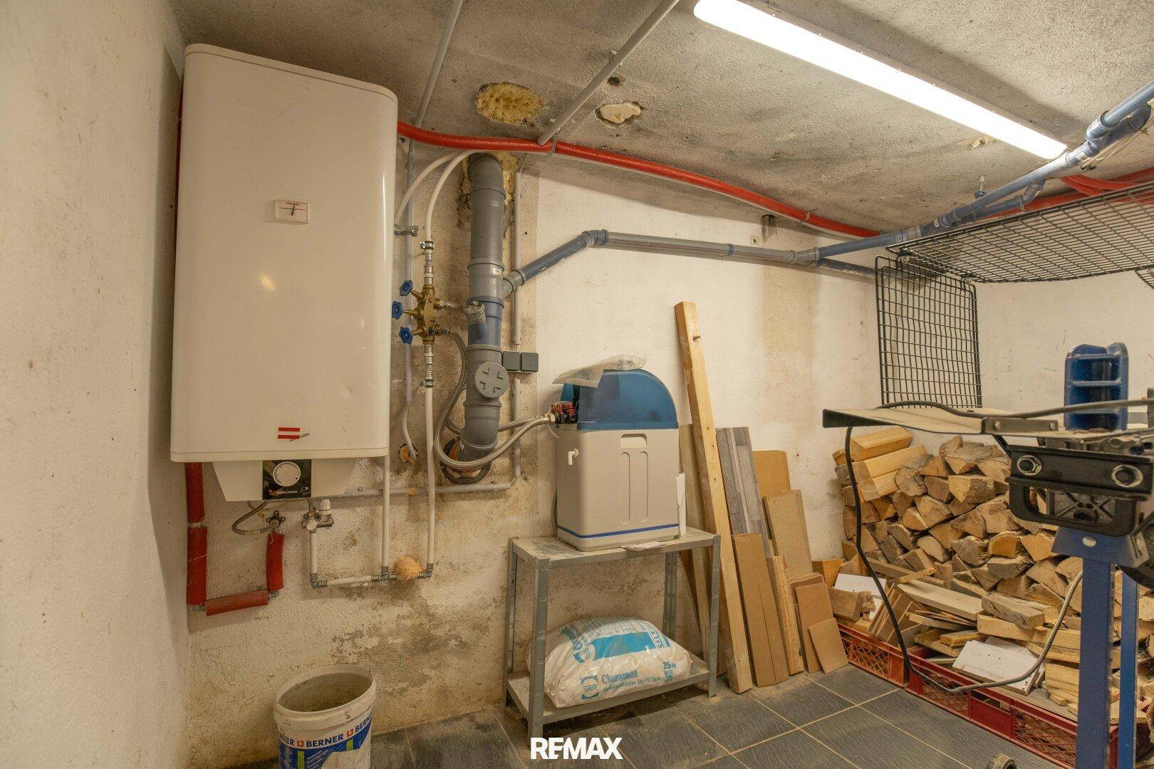 Technikraum im Keller mit Warmwasserbereiter, Wasserenthärter und Holzstapel.