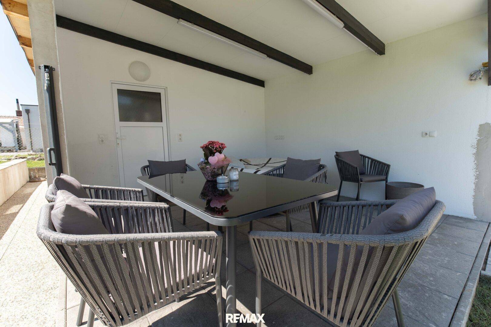 Überdachte Terrasse mit modernem Esstisch und Stühlen für Mahlzeiten im Freien.