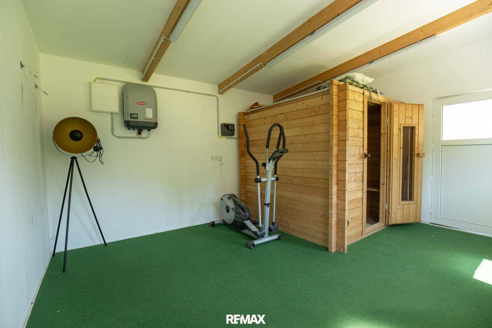 Fitnessraum mit Sauna, Trainingsgeräten und grünem Bodenbelag.