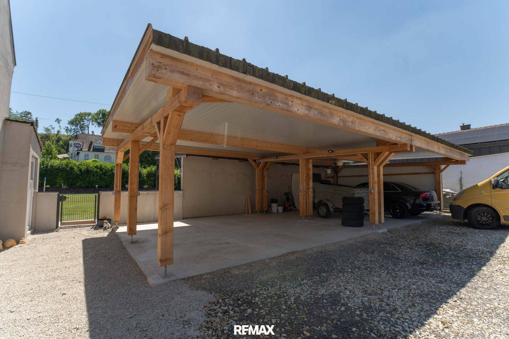 Geräumiger Holzcarport mit Platz für mehrere Fahrzeuge und Kiesauffahrt.