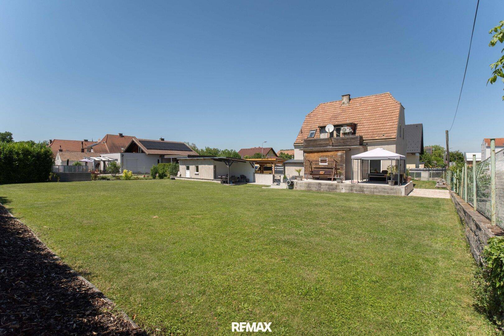 Weitläufiger Garten mit großer Rasenfläche und Blick auf das Wohnhaus mit Terrasse.