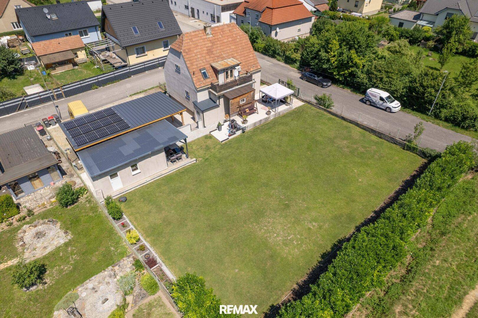 Luftaufnahme des Anwesens mit großem Garten, Wohnhaus und Nebengebäuden unter blauem Himmel.